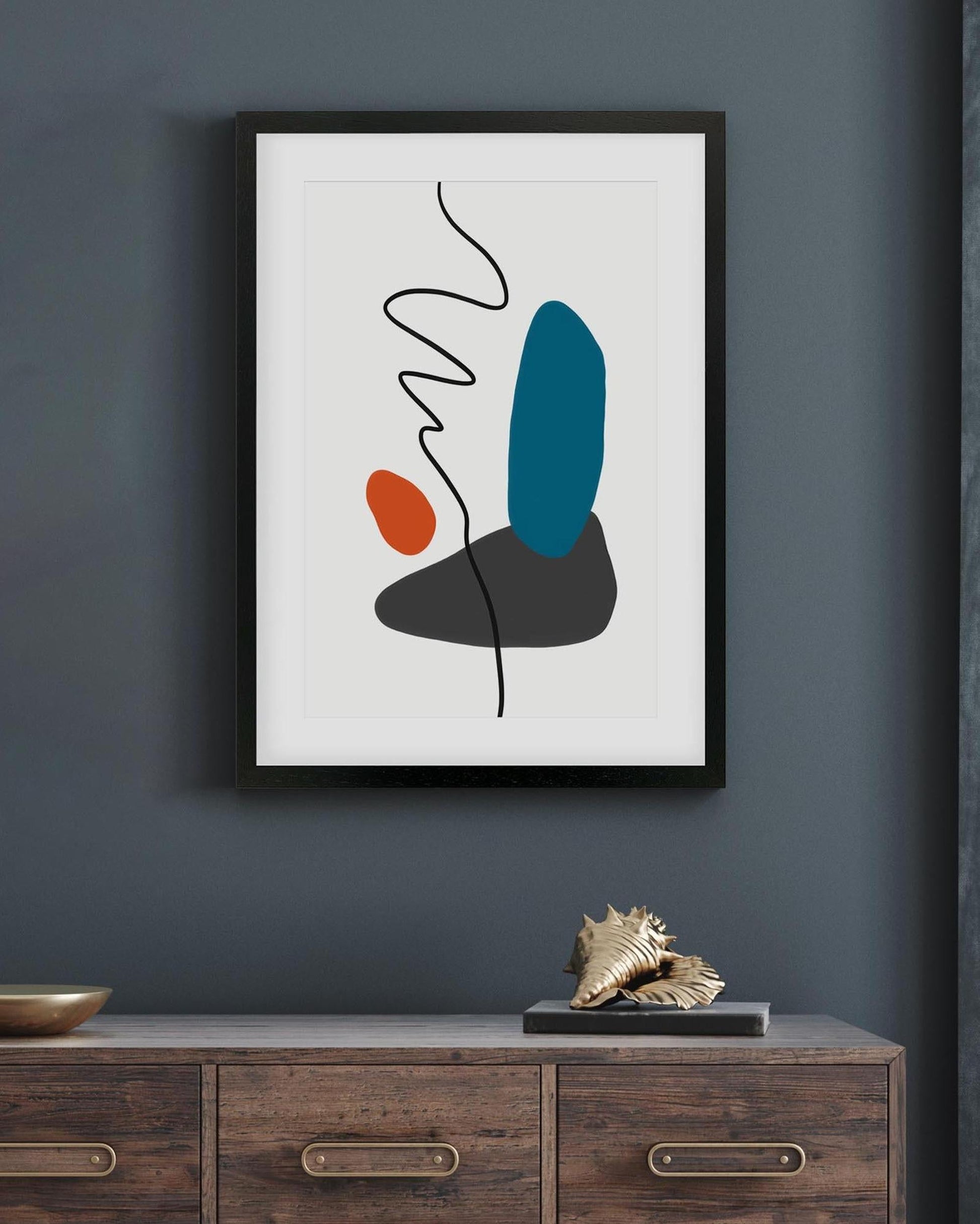 Framed abstract art print on a dark wall above a wooden cabinet.