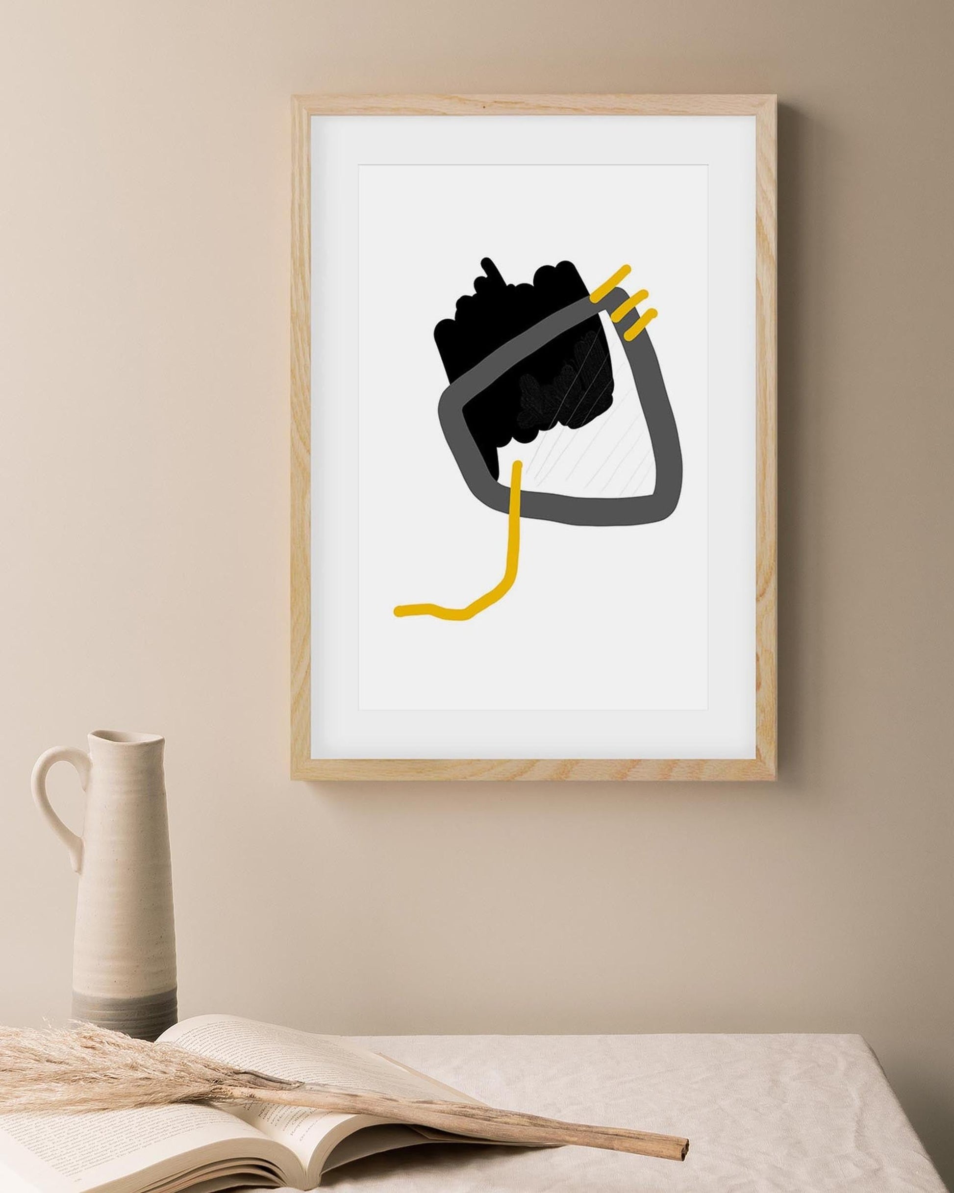 Framed abstract art print on a beige wall with a vase and book in the foreground.