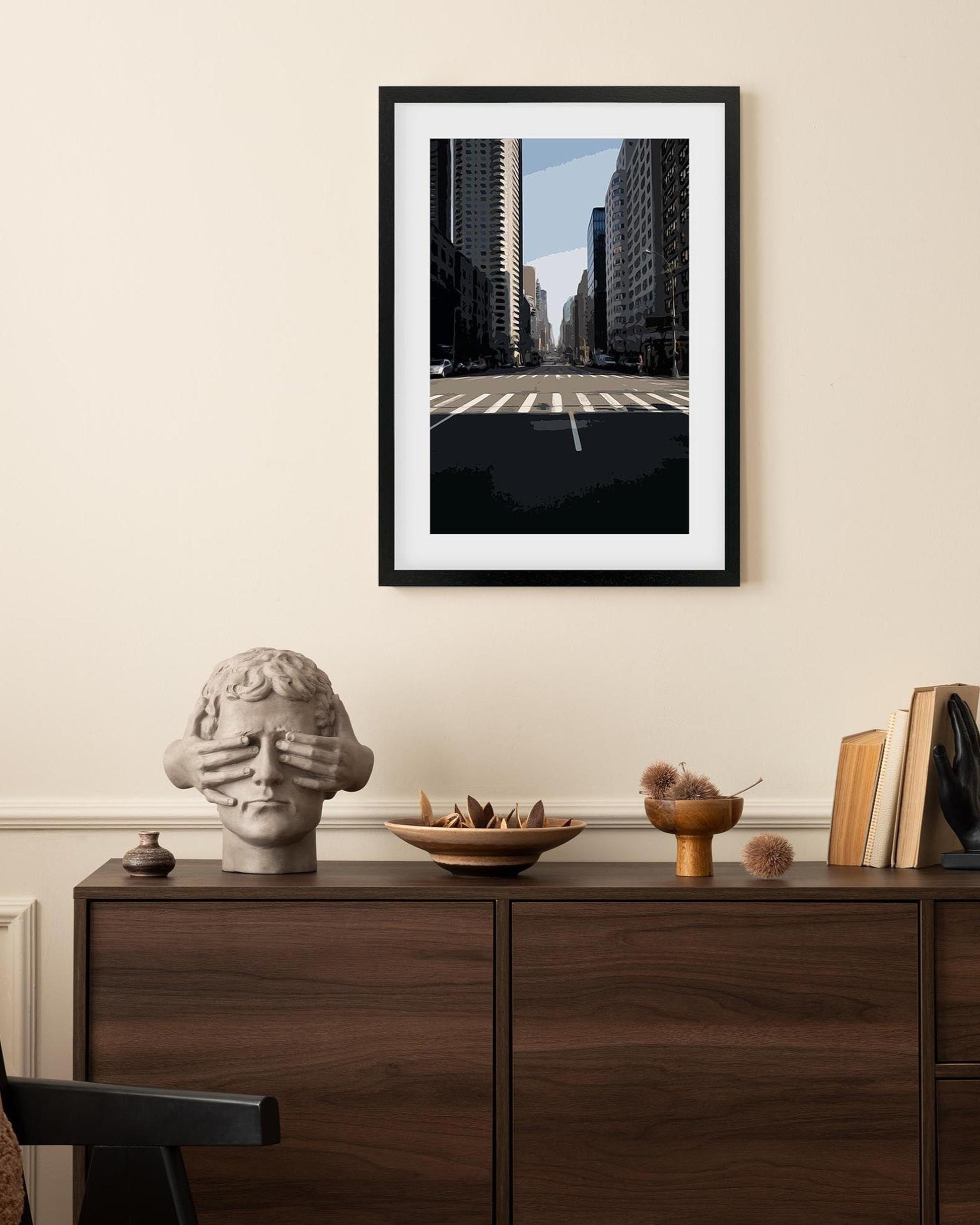 Framed cityscape print on a wall above a wooden cabinet with decorative items.