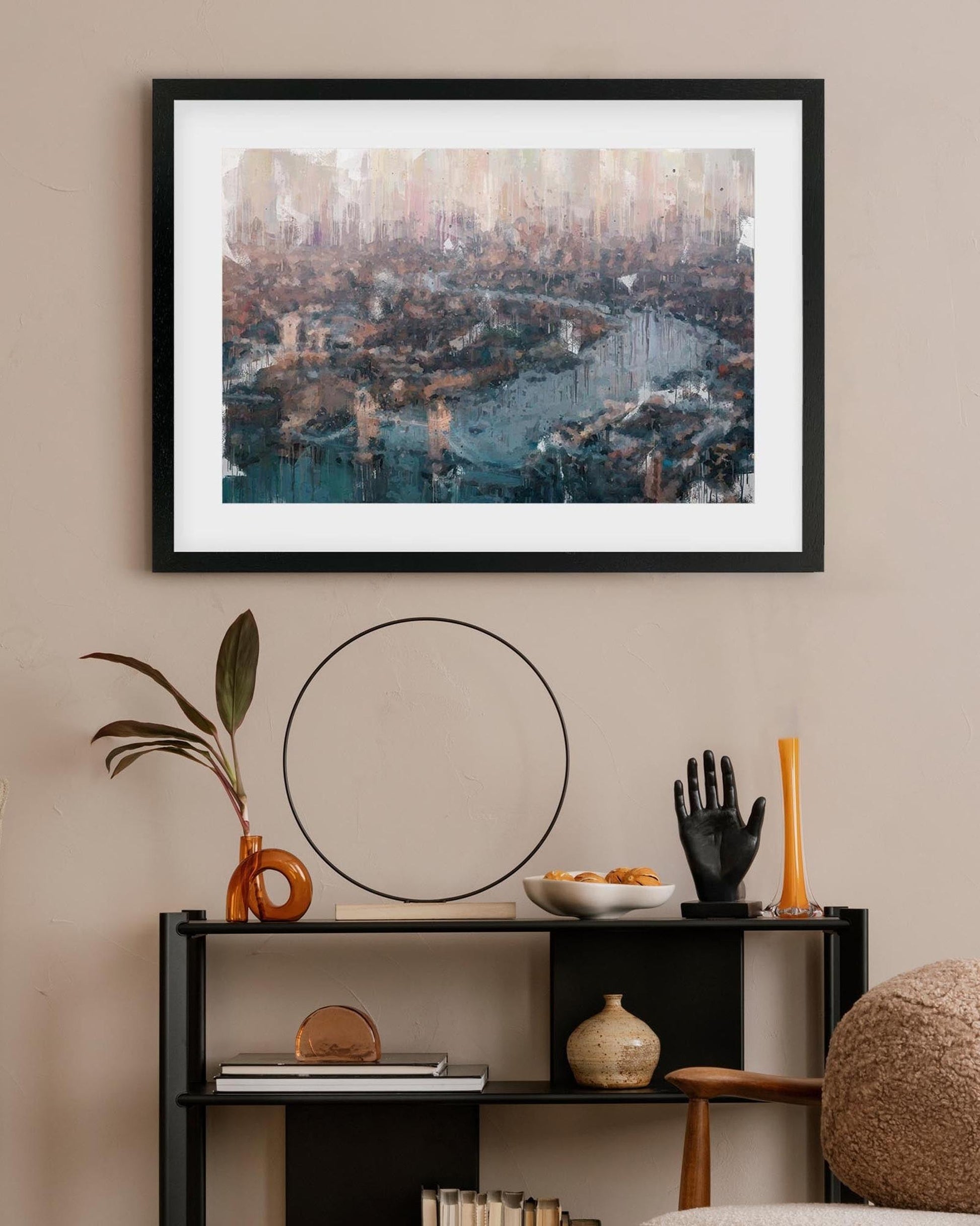 Framed cityscape art above a shelf with decorative items on a beige wall.