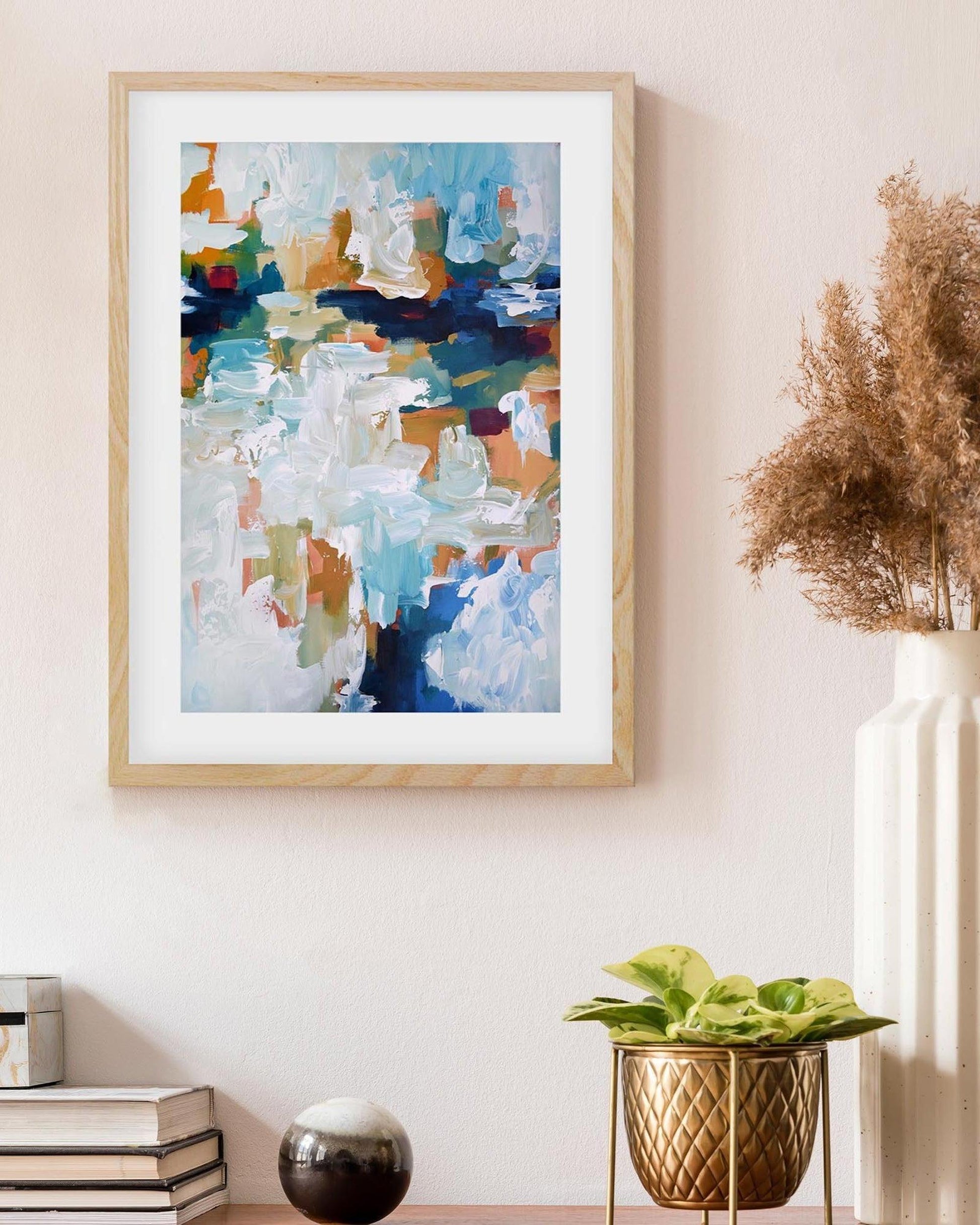Abstract art print in a wooden frame on a wall with decorative vases and plants.