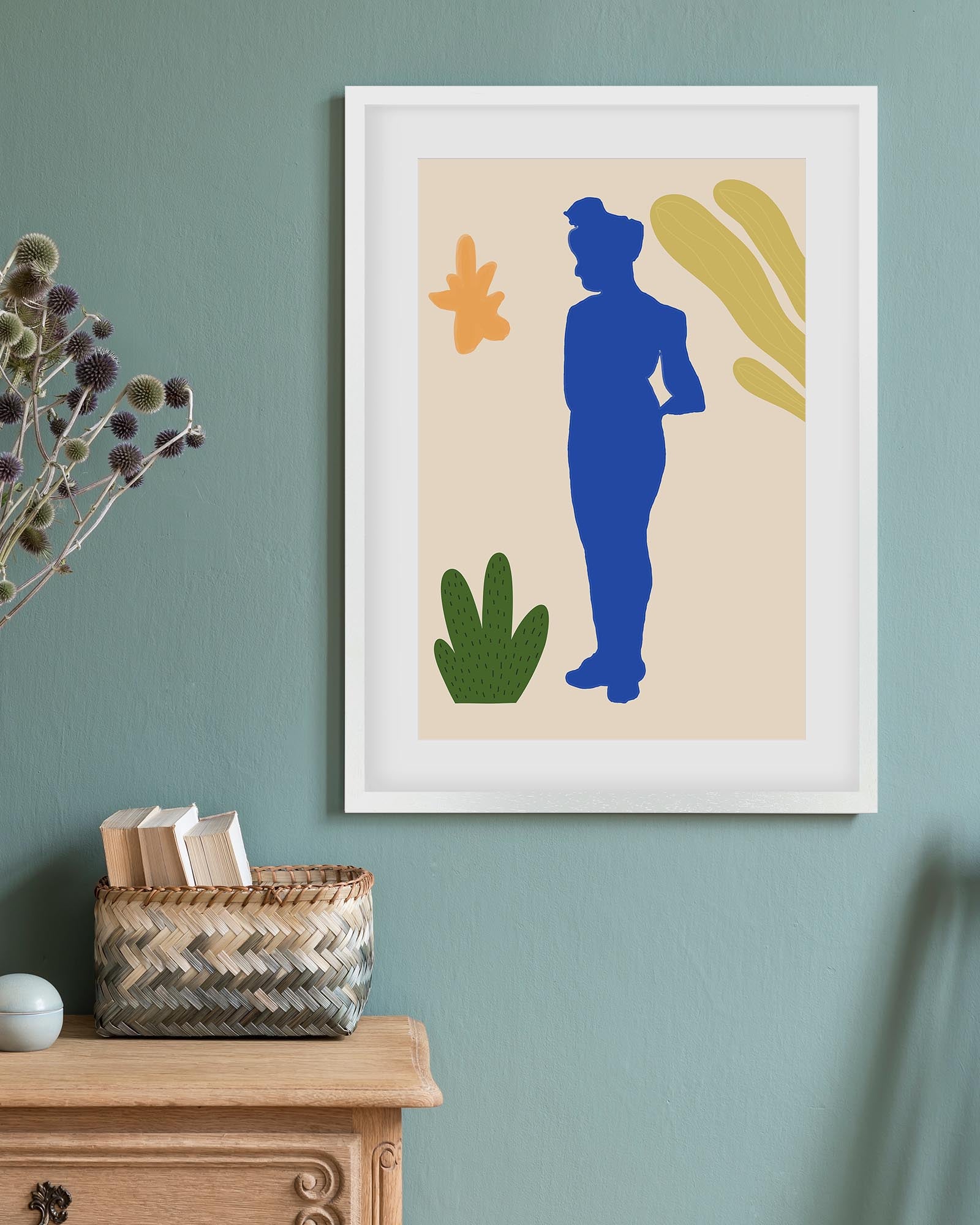 Framed abstract art print with a blue silhouette on a beige background, displayed on a wall above a wooden cabinet.