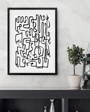 Framed abstract black line art on a white wall with a plant and lantern in the background.