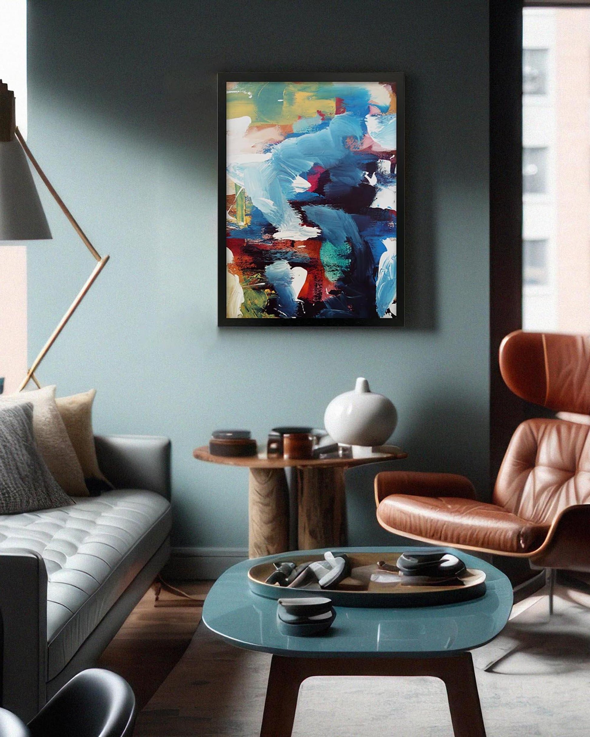 Modern living room with a colorful abstract painting on the wall, a gray sofa, brown armchair, and a round glass coffee table.