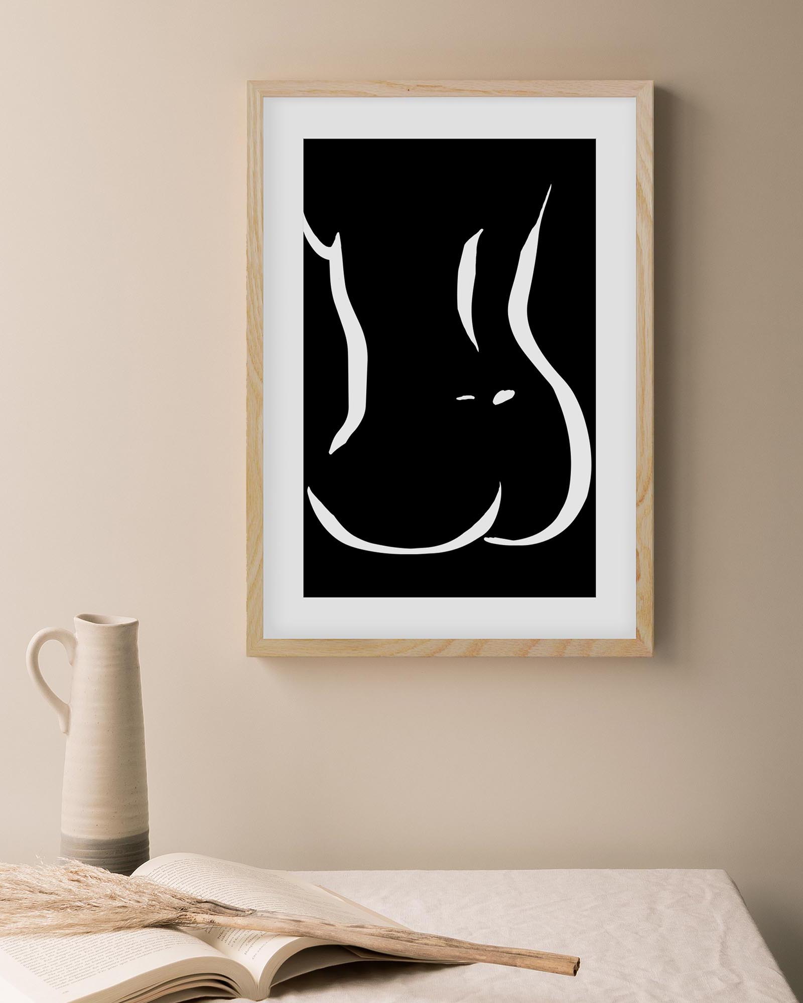 Framed black and white abstract art print on a beige wall with a vase and book in the foreground.