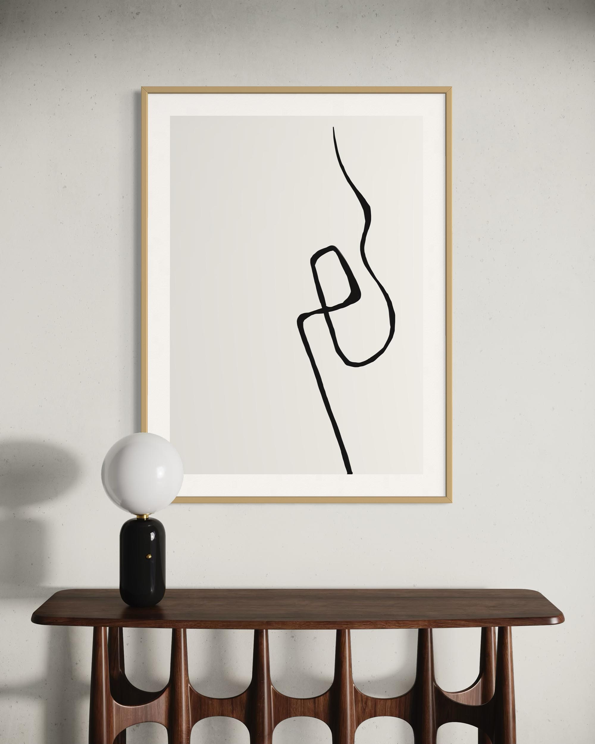Framed abstract line art on a wall above a wooden console table with a decorative lamp.