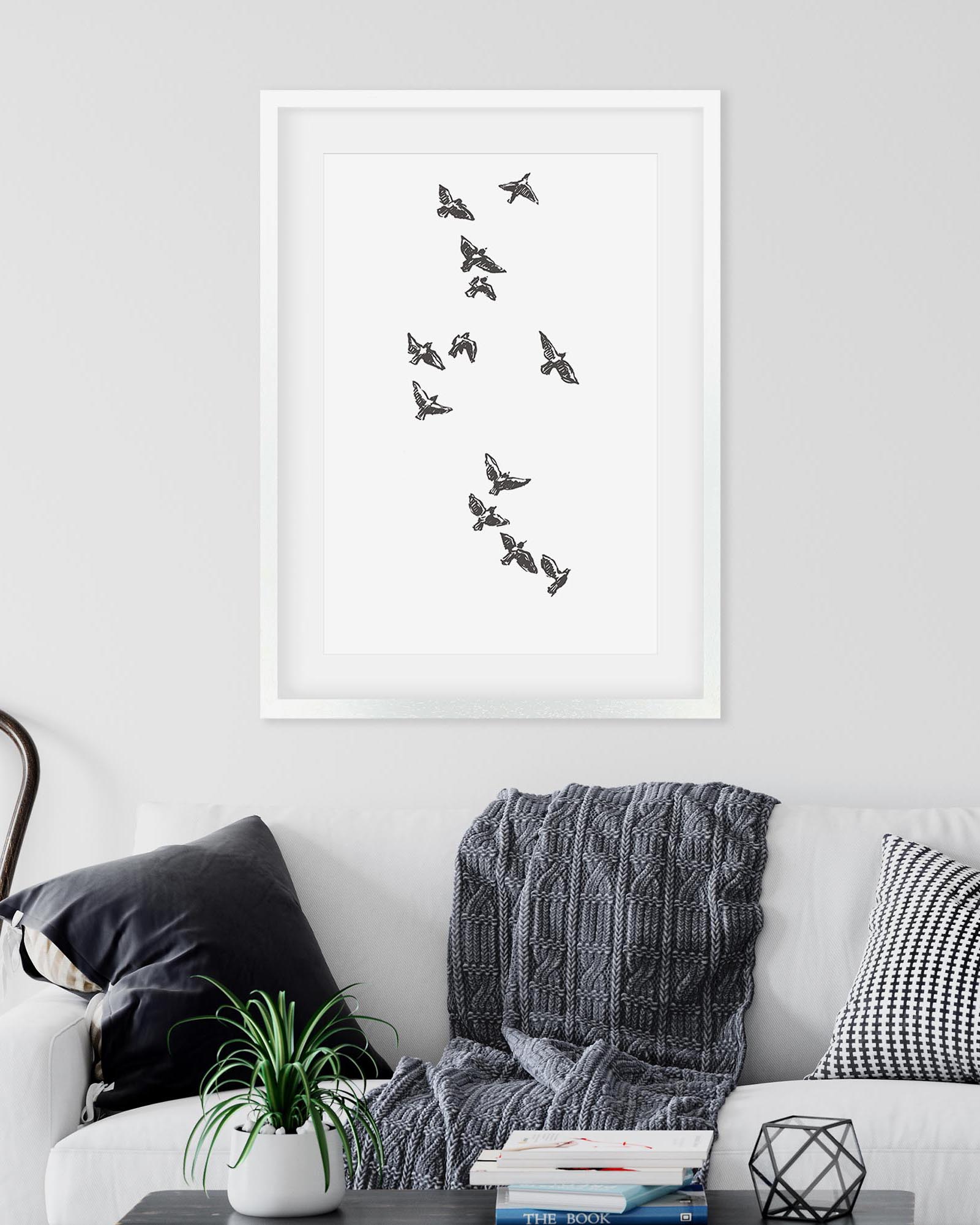 Framed butterfly art print on a wall above a sofa with decorative pillows and a plant.