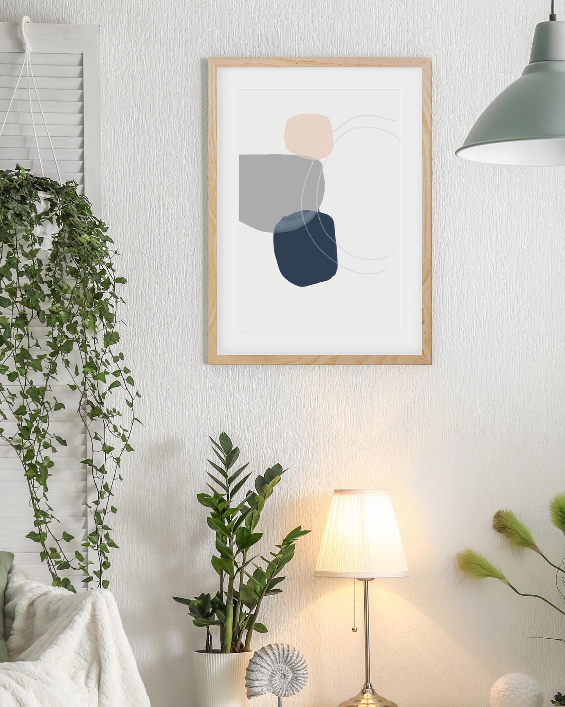 Framed abstract art print on a wall with plants and a lamp in a room.