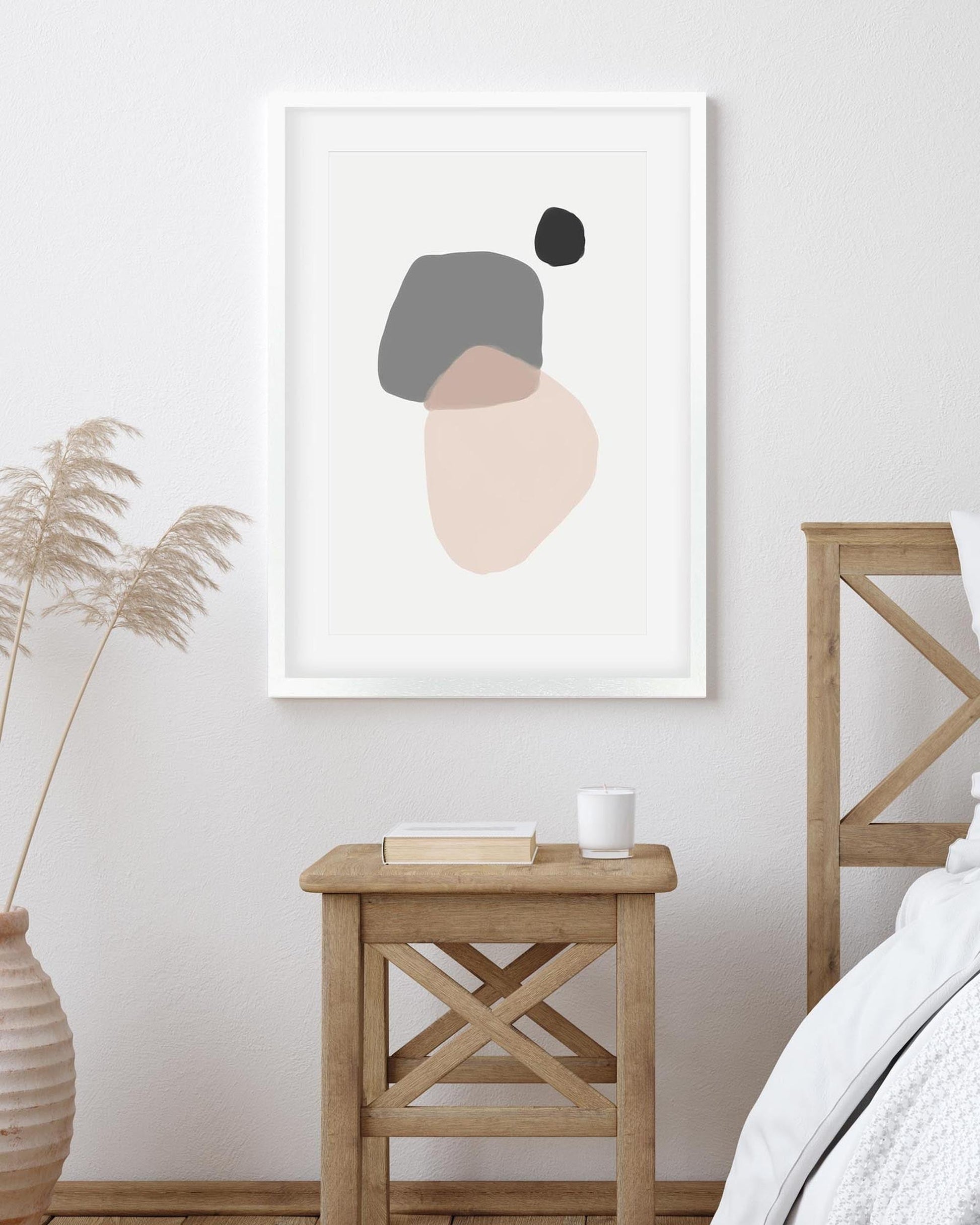 Framed abstract art print on a wall above a wooden side table with a plant and mug.