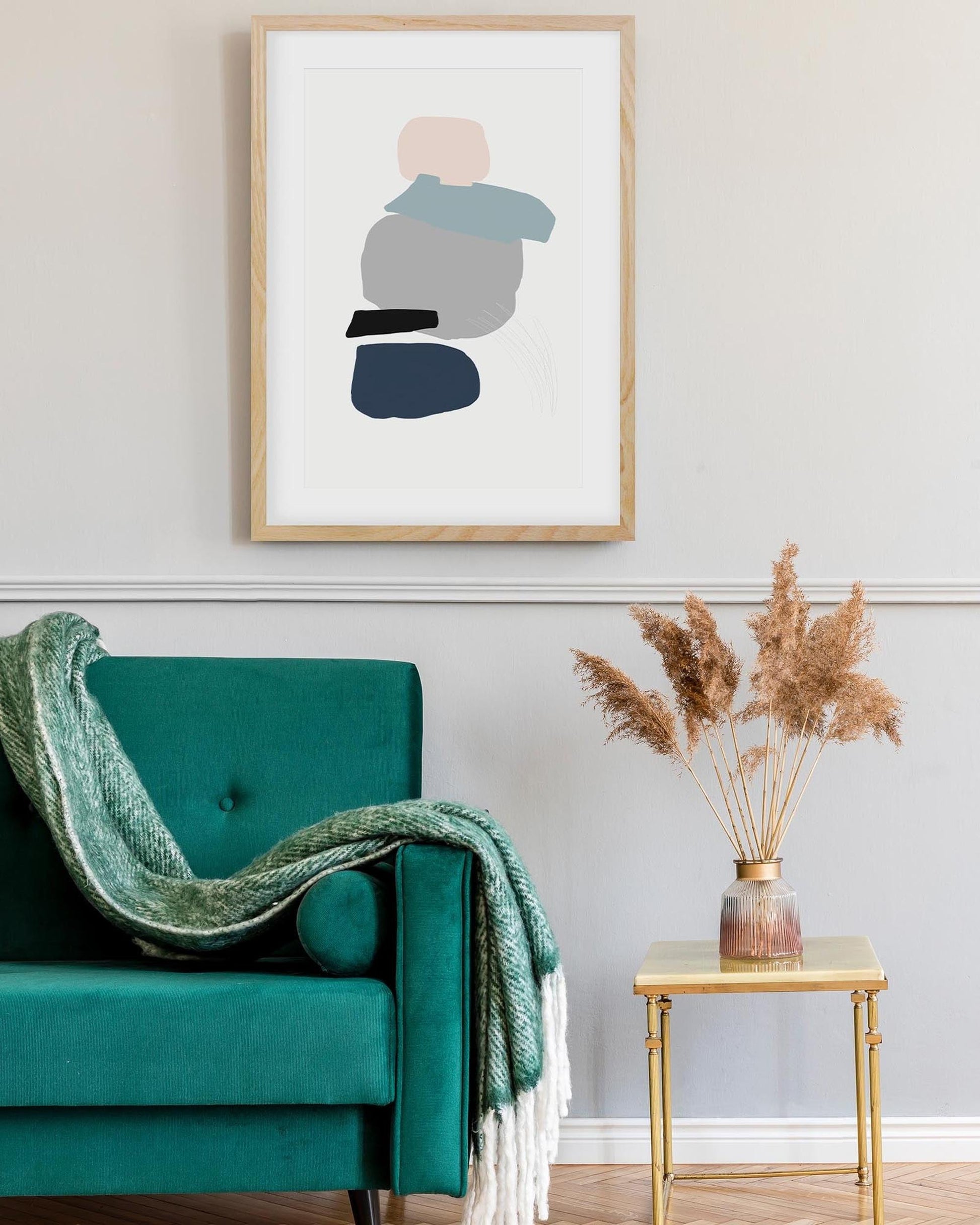 Teal armchair with a green blanket, gold side table with dried plants, and abstract art on the wall.
