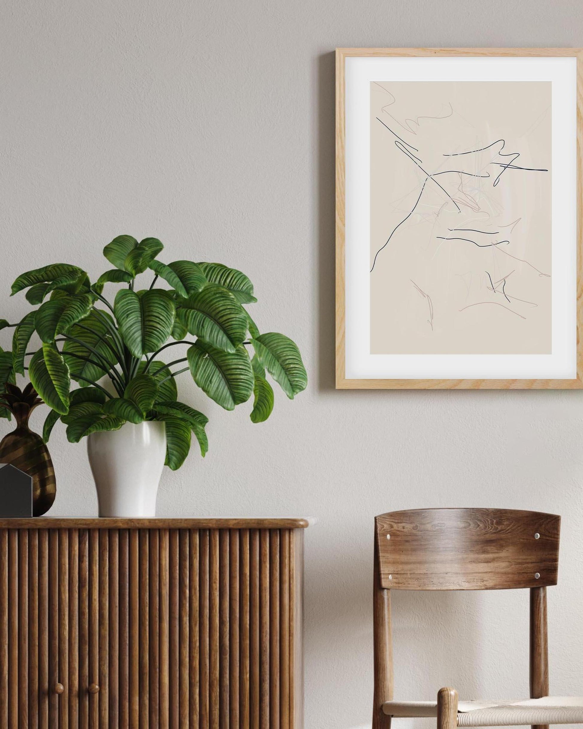 Framed abstract art on a wall with a plant and wooden furniture in the foreground.
