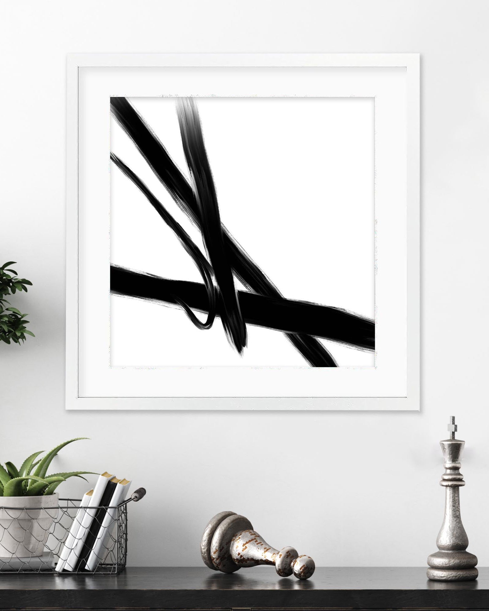 Framed black and white abstract art print on a wall with decorative items below.