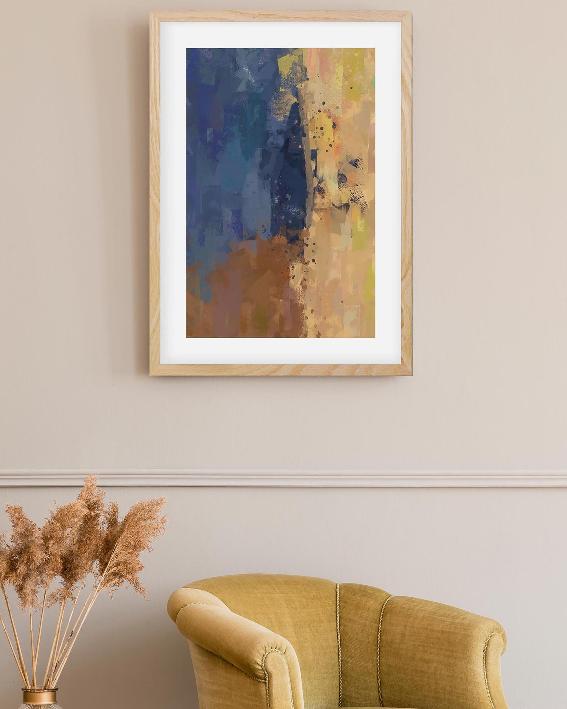 Framed abstract art piece on a wall above a yellow armchair with pampas grass decor.