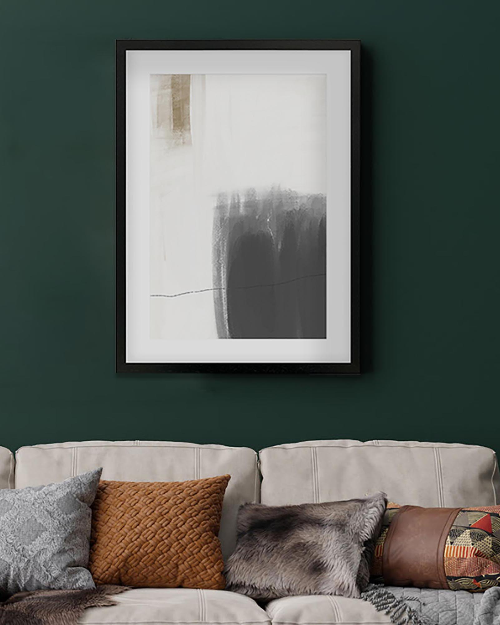 Framed abstract art piece on a dark green wall above a beige sofa with patterned cushions.