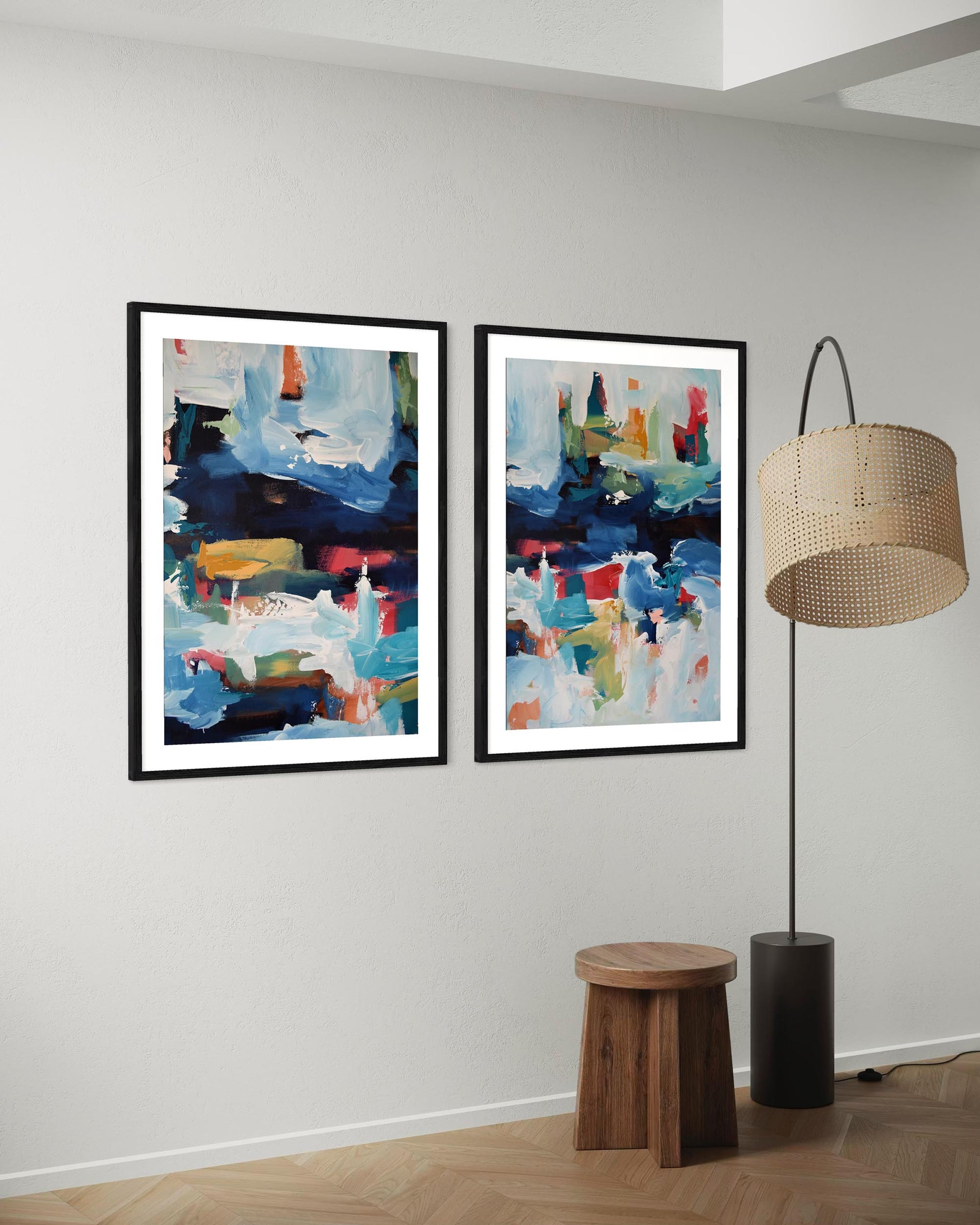 Two abstract art pieces on a wall with a wooden stool and floor lamp.