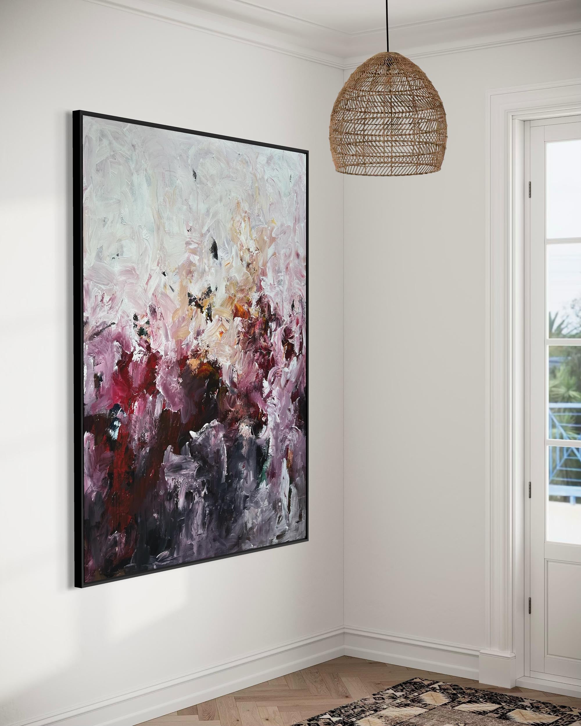 Abstract painting on a wall in a room with a woven pendant light and a door leading outside.