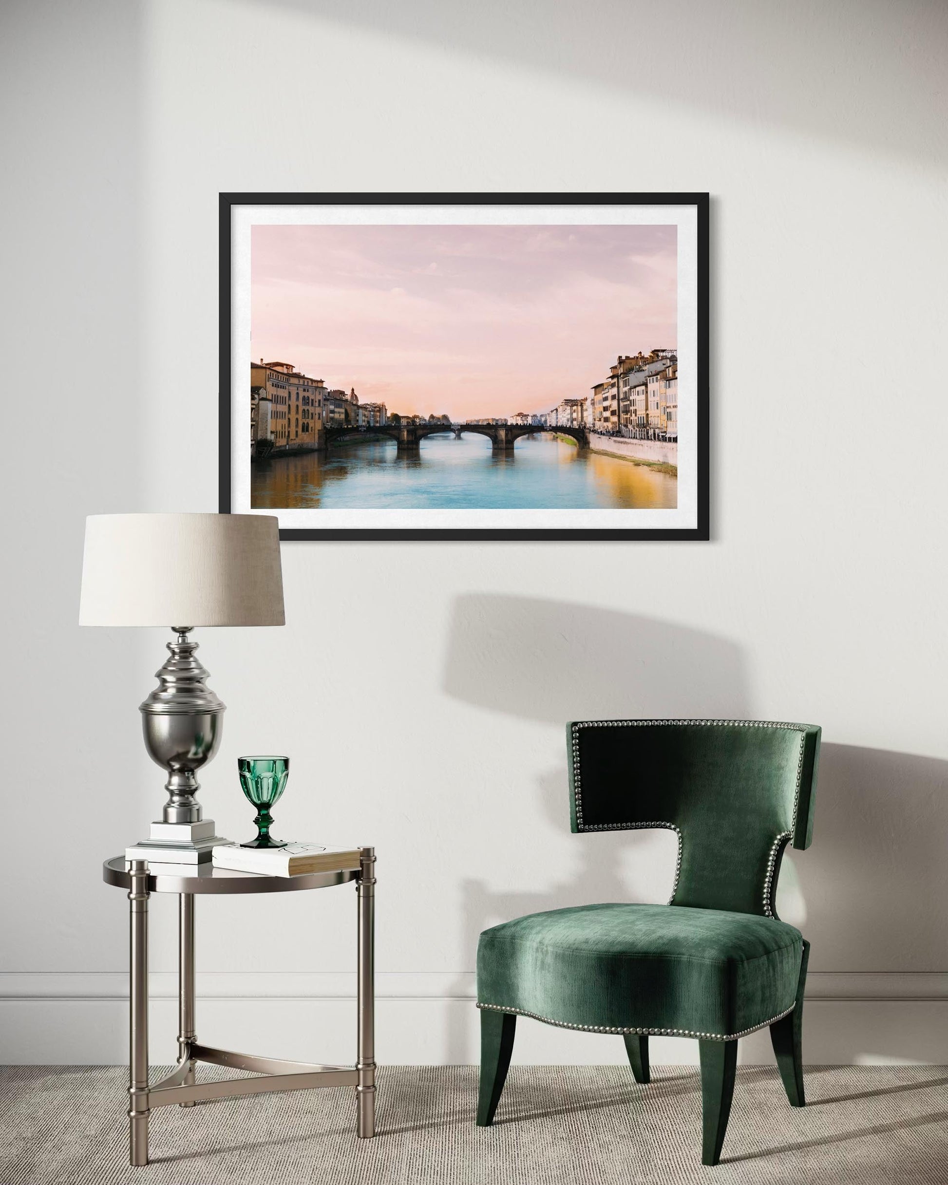 Green chair and side table with a framed artwork of a cityscape on a white wall.