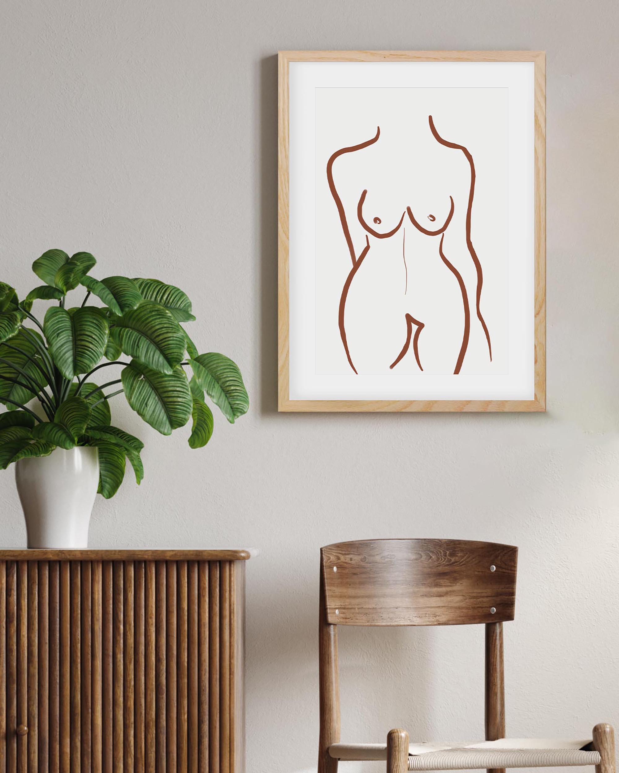 Framed abstract artwork of a nude figure on a wall with a plant and chair in the foreground.