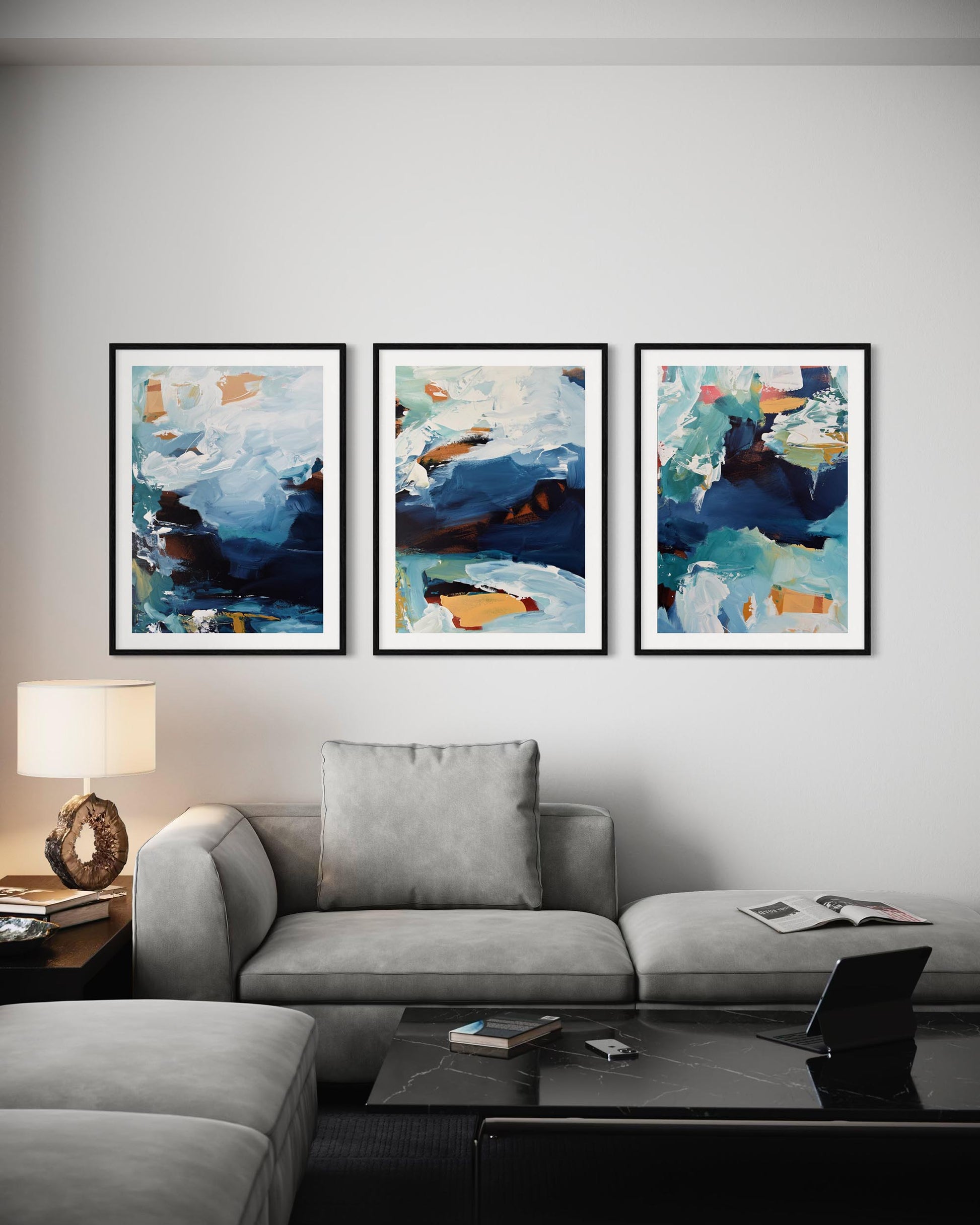 Three abstract paintings on a wall above a gray sofa in a living room.