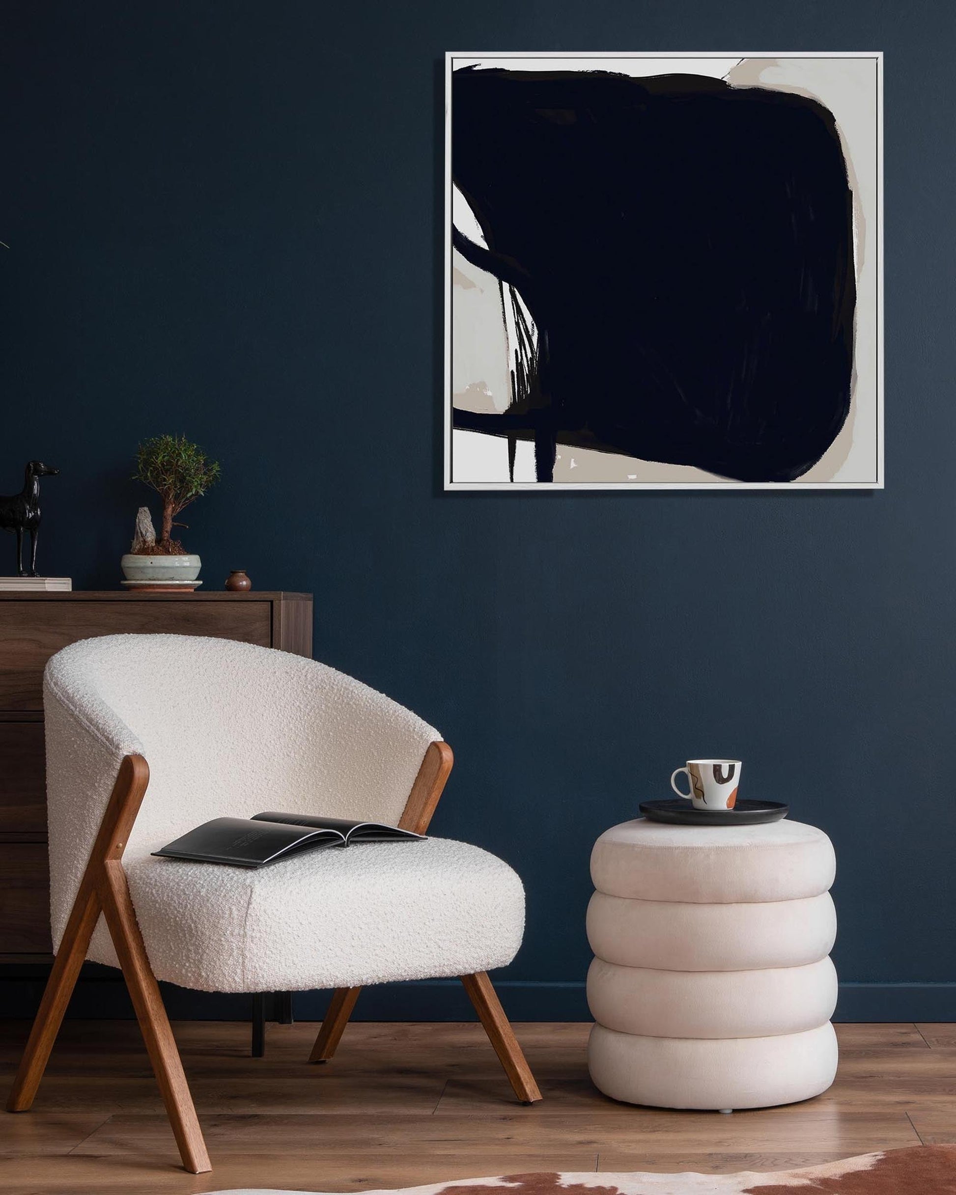 Modern interior with a white armchair, wooden sideboard, and abstract art on a dark wall.