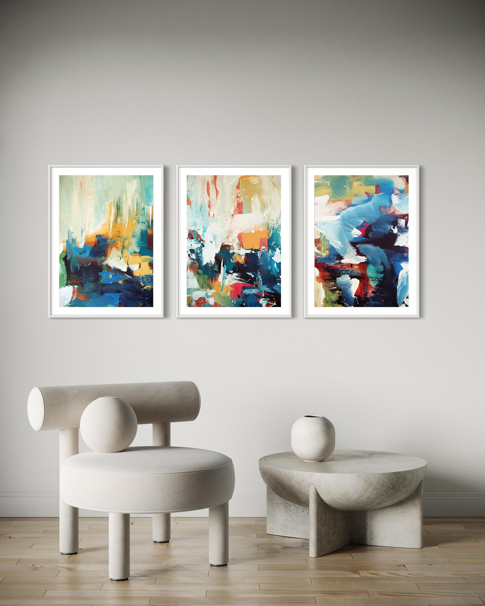 Three abstract paintings on a wall with a modern chair and table below.