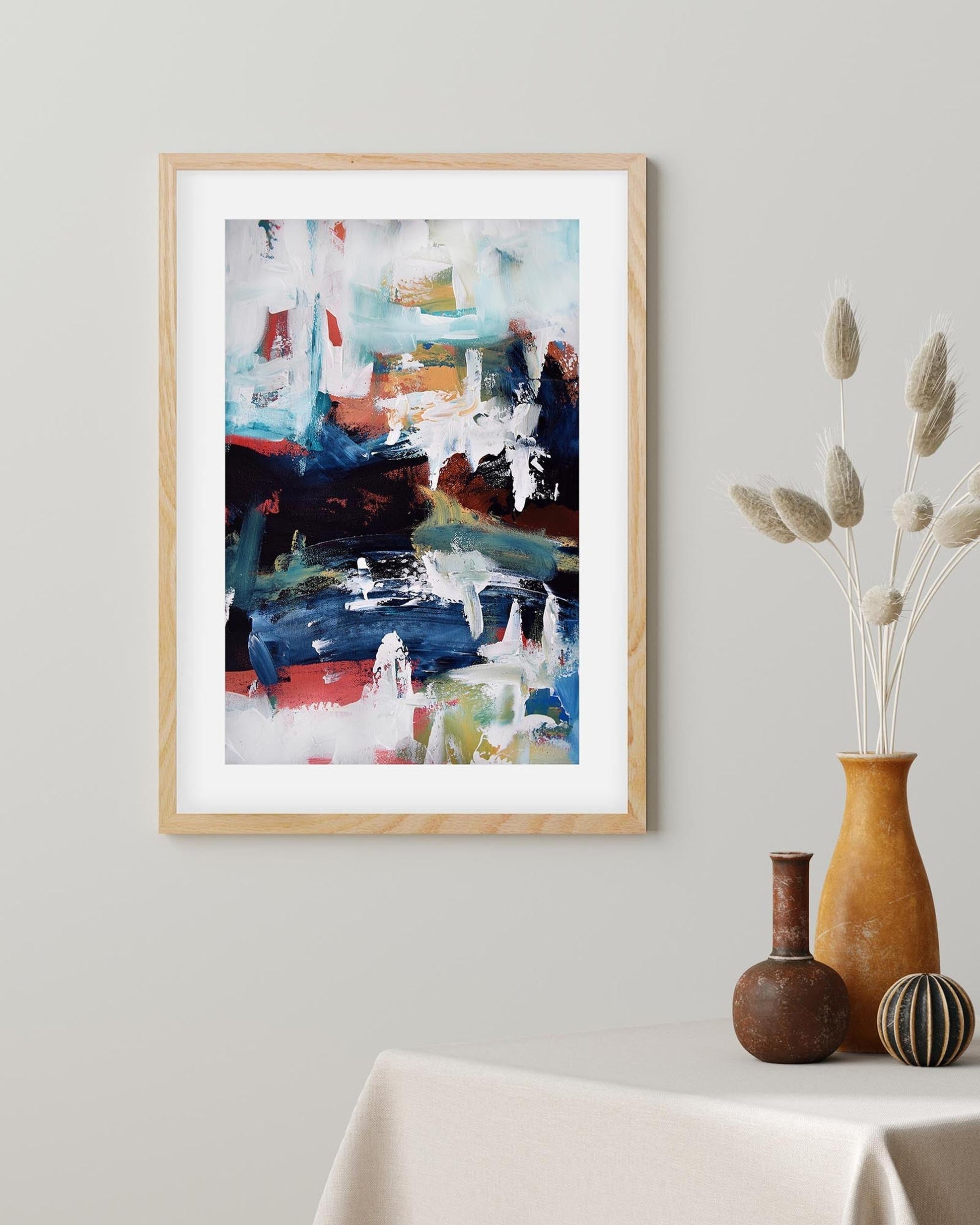 Framed abstract art on a wall with decorative vases below.