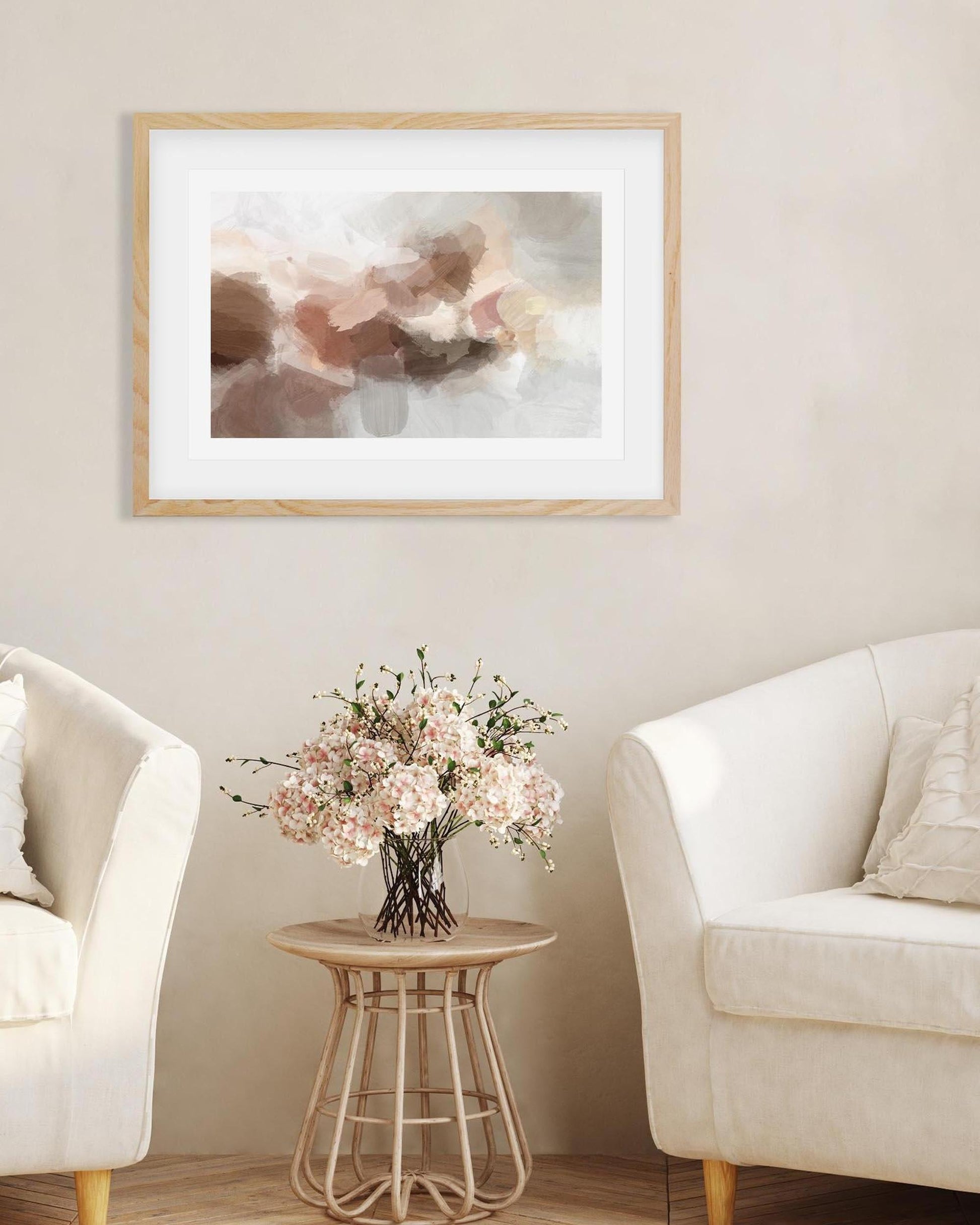 Framed abstract art piece on a wall above a small table with flowers, flanked by two white chairs.