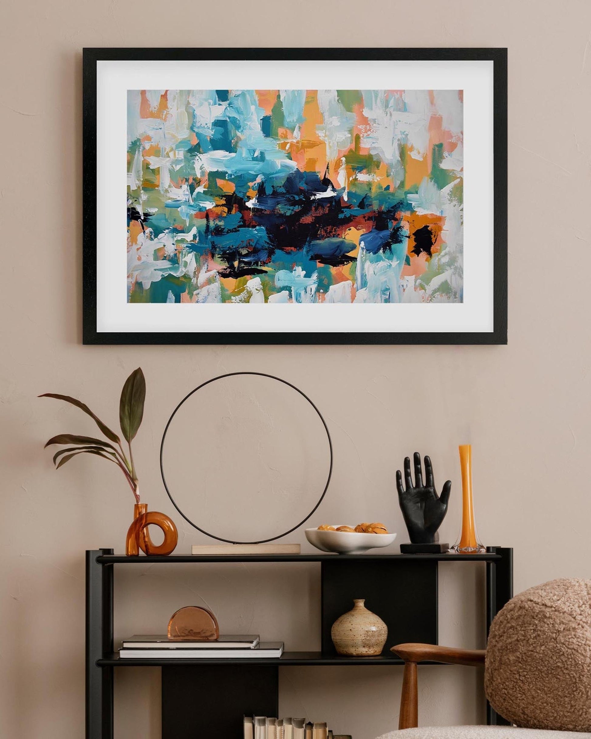 Framed abstract art piece on a wall above a shelf with decorative items.