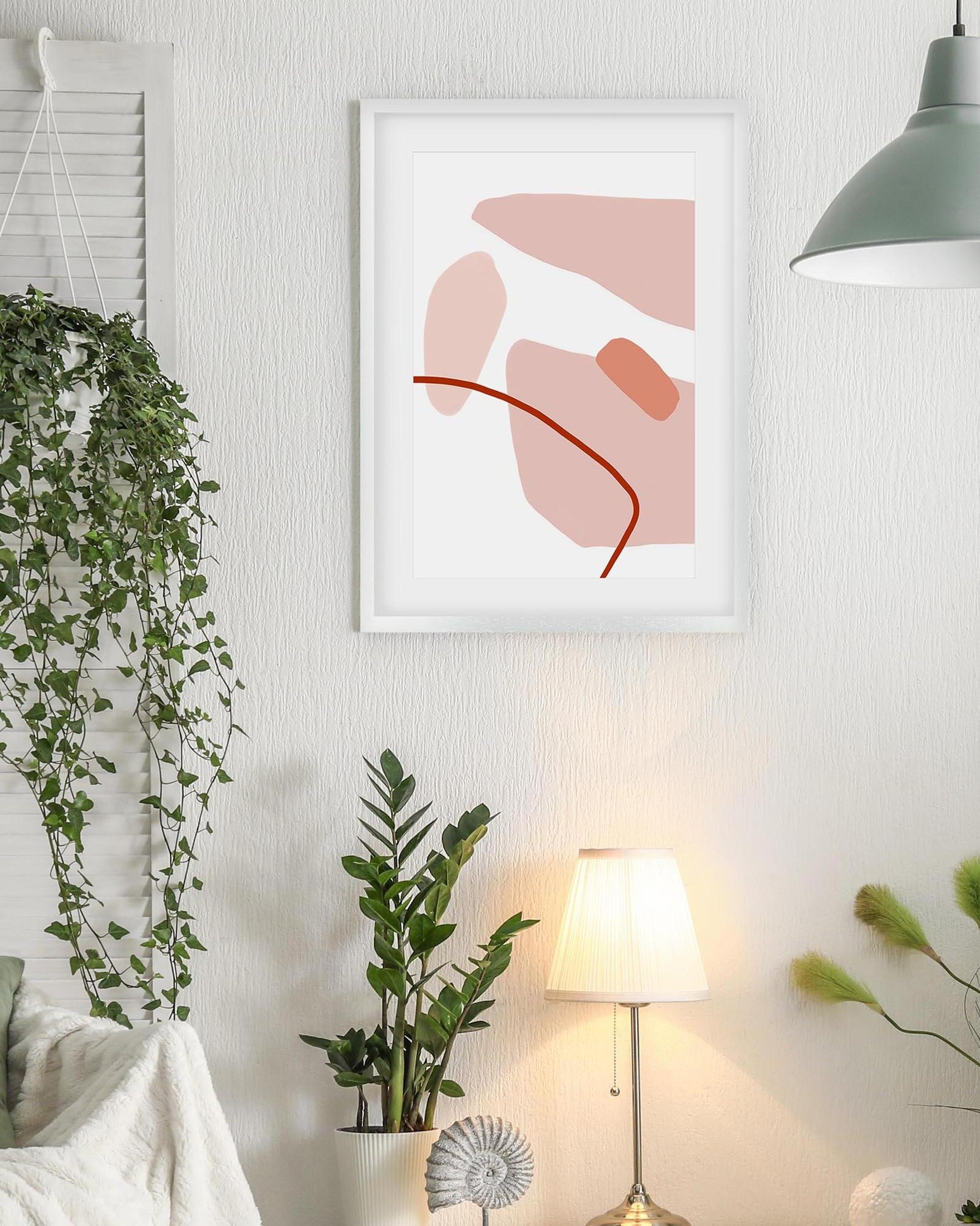 Framed abstract art on a wall with plants and a lamp in a room.