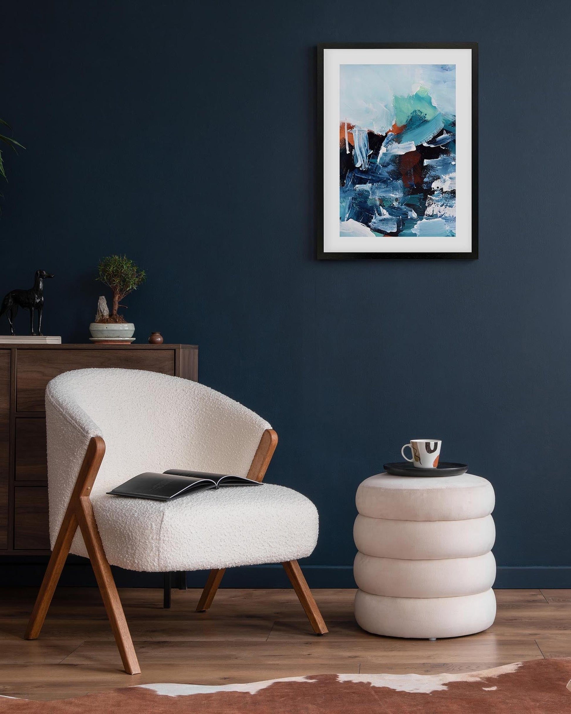 Modern living room with a white armchair, side table, and abstract art on a dark blue wall.