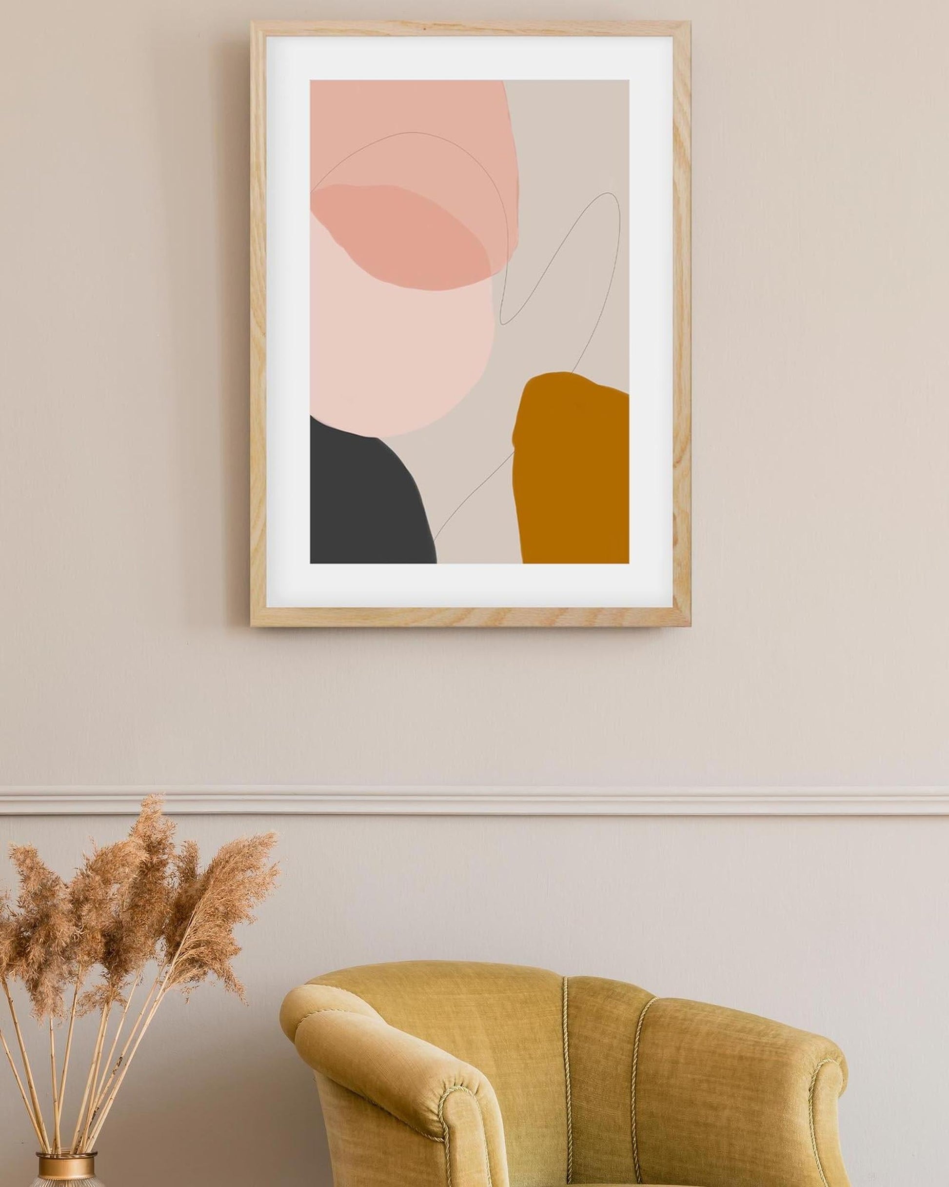 Abstract art print in a wooden frame on a wall above a yellow armchair.
