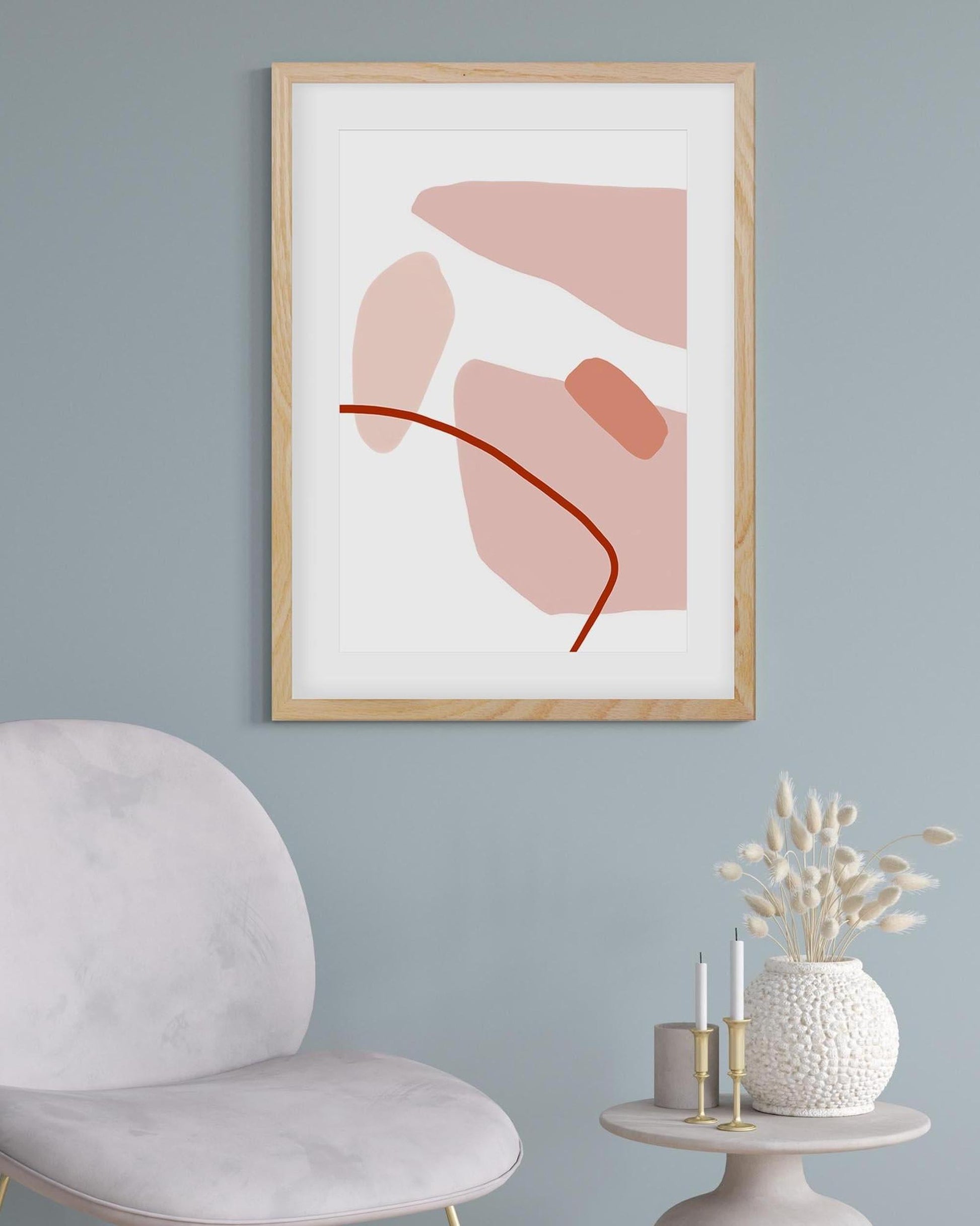 Framed abstract art print on a wall with a chair and decorative items below.