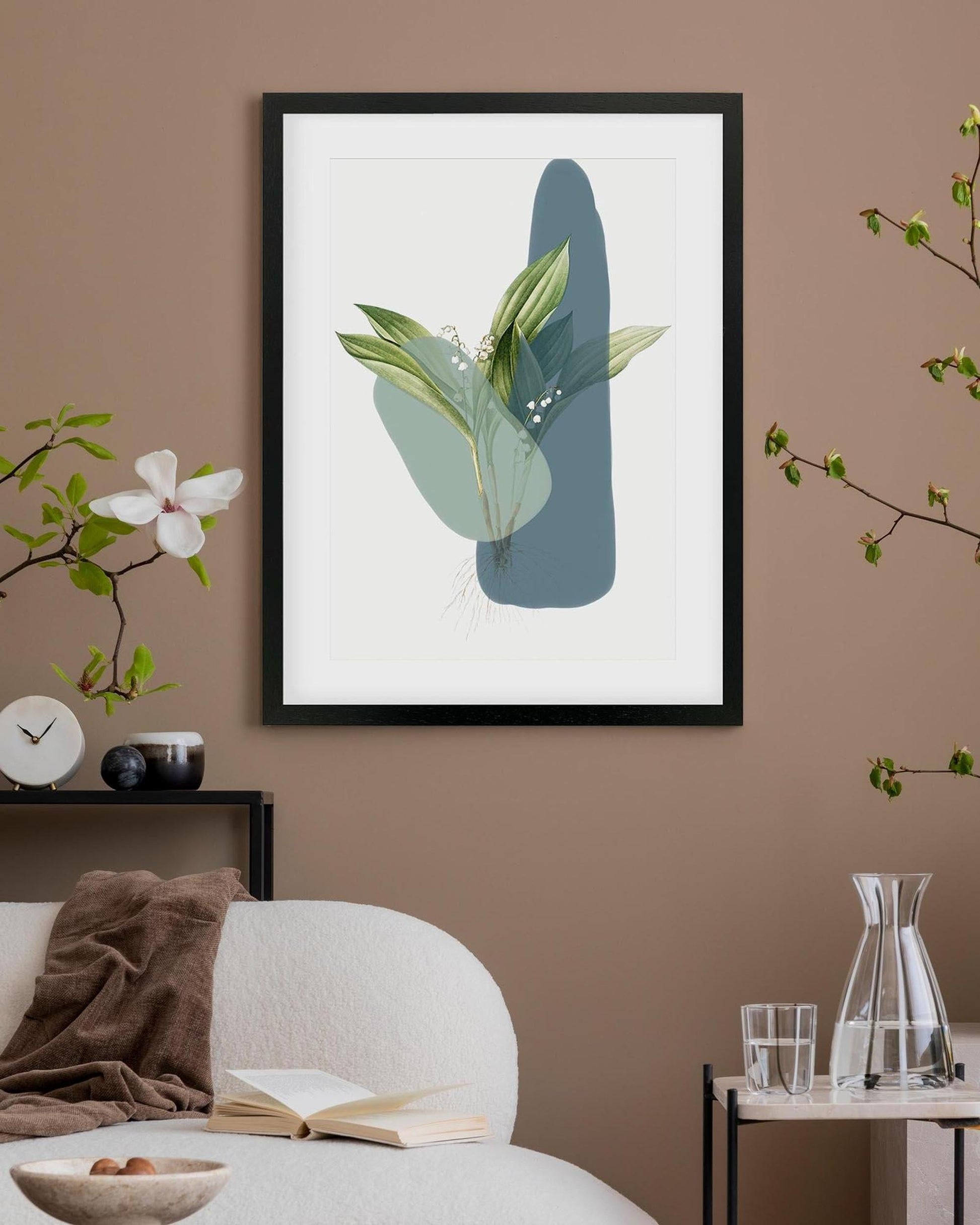 Framed artwork with green leaves on a beige wall above a sofa.