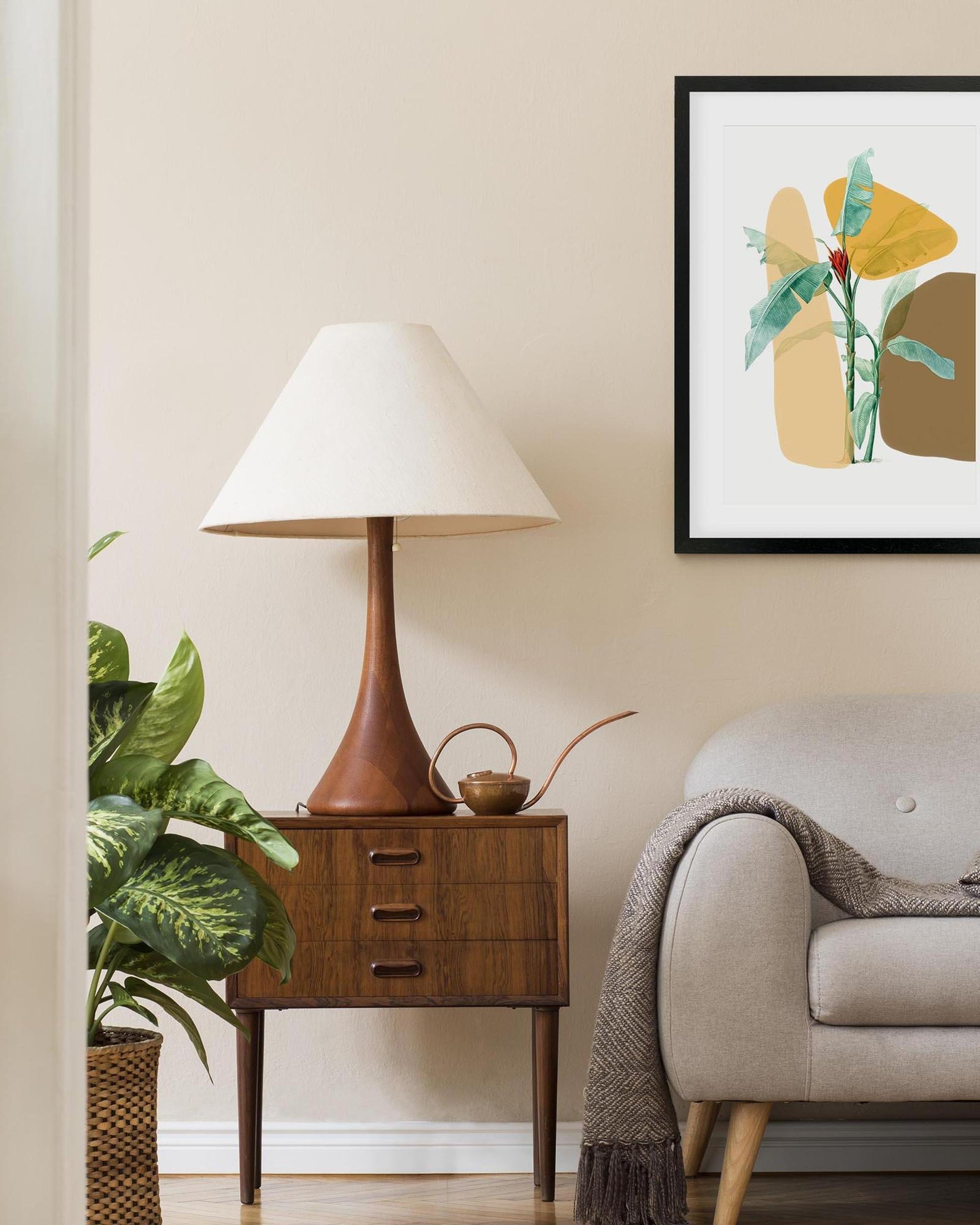 Nest living room with a lamp on a wooden side table, plant, and abstract art on the wall.
