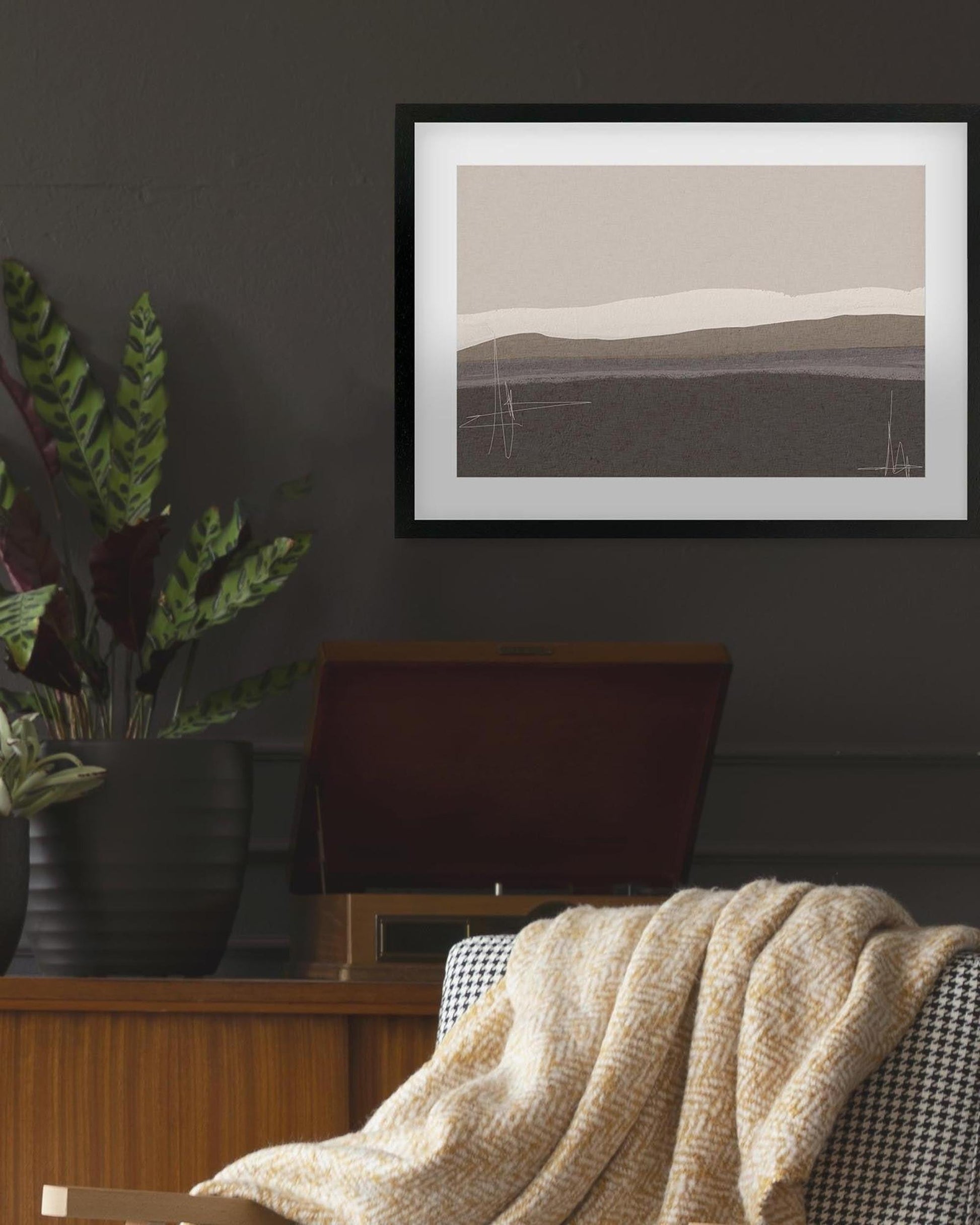 Framed landscape print on a wall above a chair with a blanket