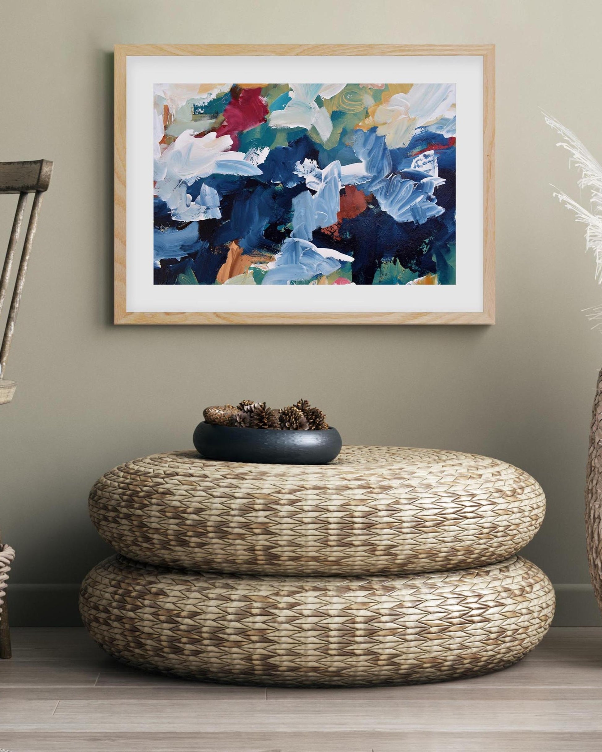 Woven ottoman with a decorative bowl in a room with a framed abstract painting on the wall.
