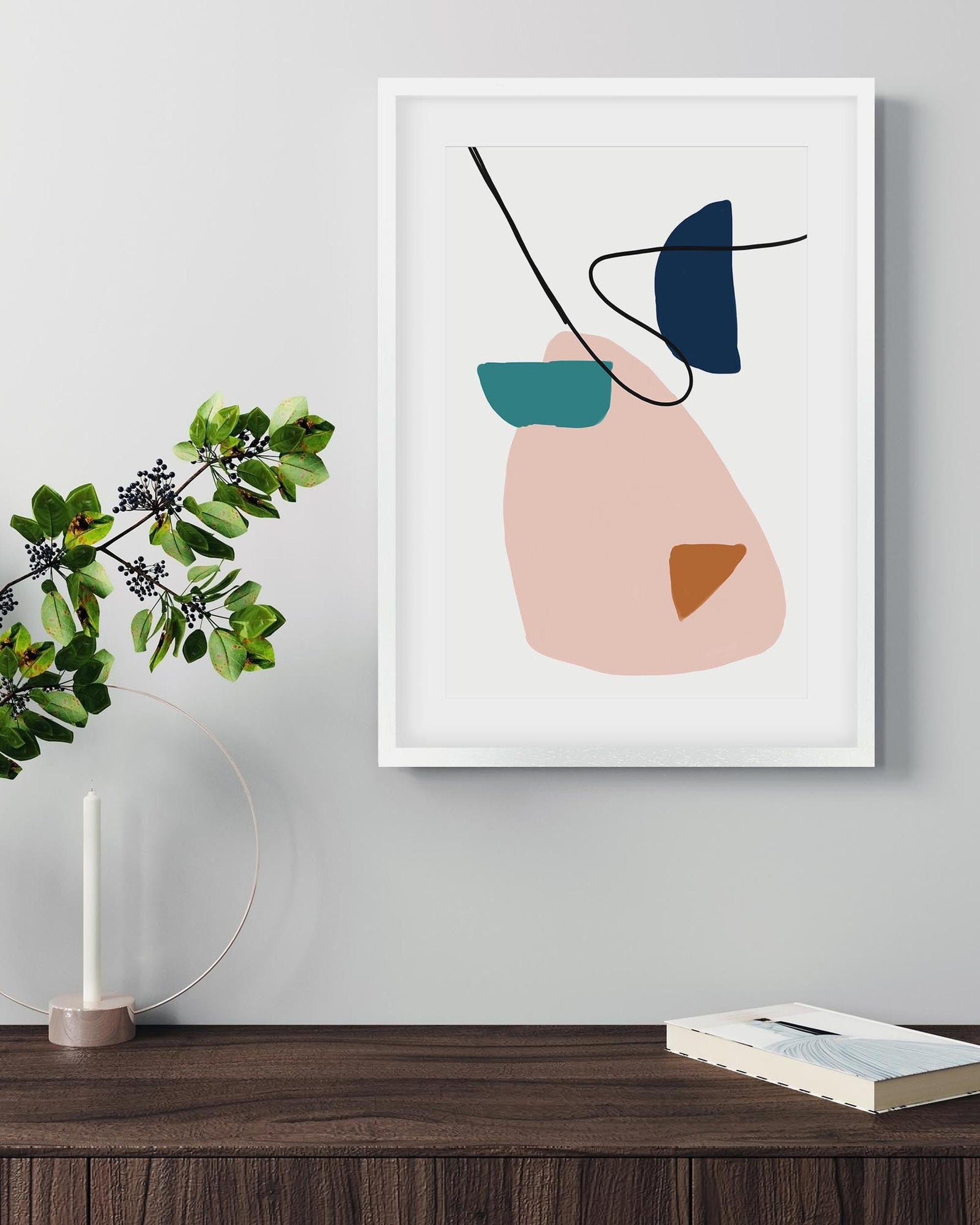 Abstract art print on a wall with a plant and books on a wooden surface.