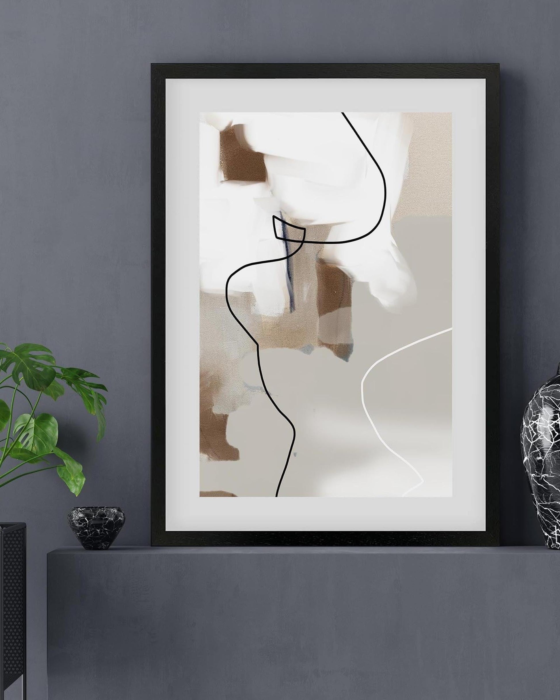 Framed abstract art piece on a gray wall with a plant and decorative object.