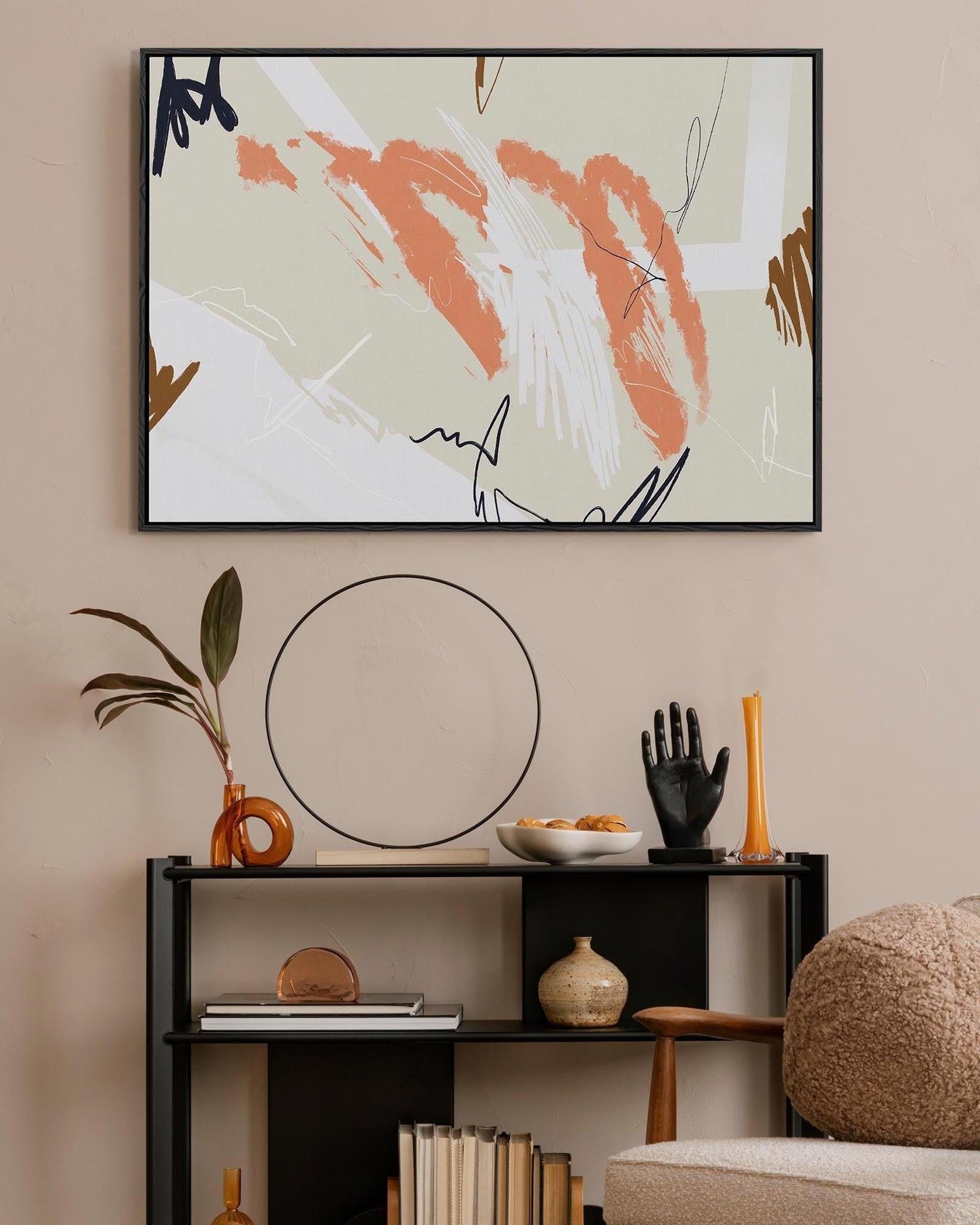 A vibrant abstract composition framed canvas hanging on a wall above a bookshelf, with a black frame and beige background.