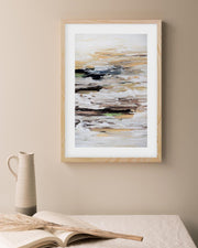 Framed abstract art piece on a beige wall with a vase and book in the foreground.