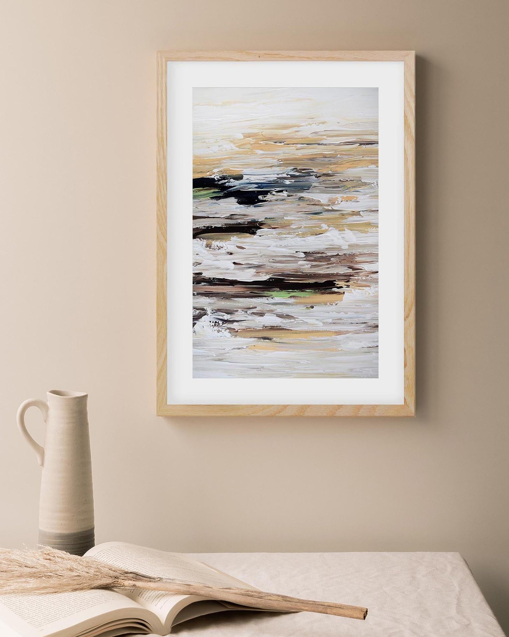 Framed abstract art piece on a beige wall with a vase and book in the foreground.