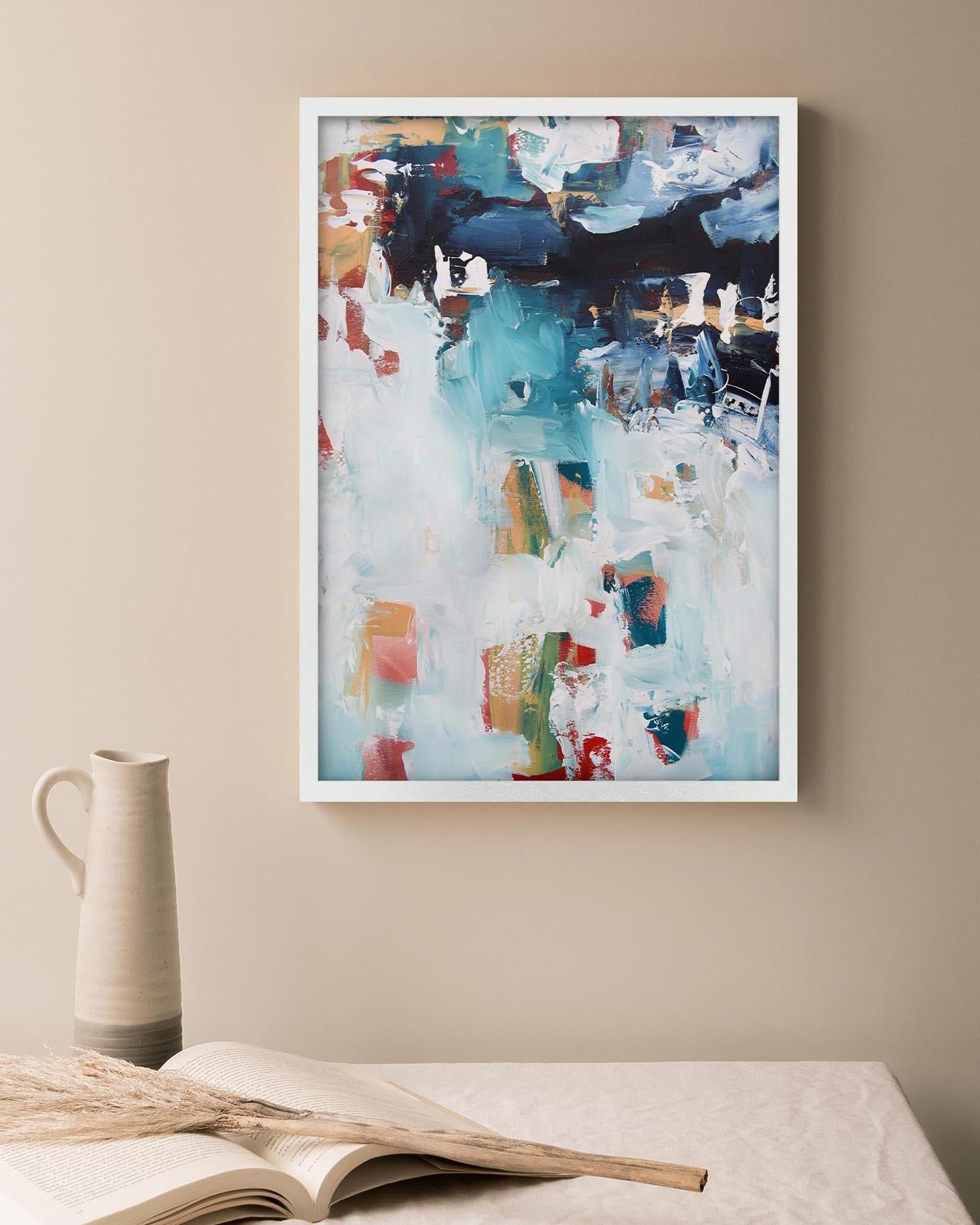 Abstract art print on a wall above a table with a book and vase.