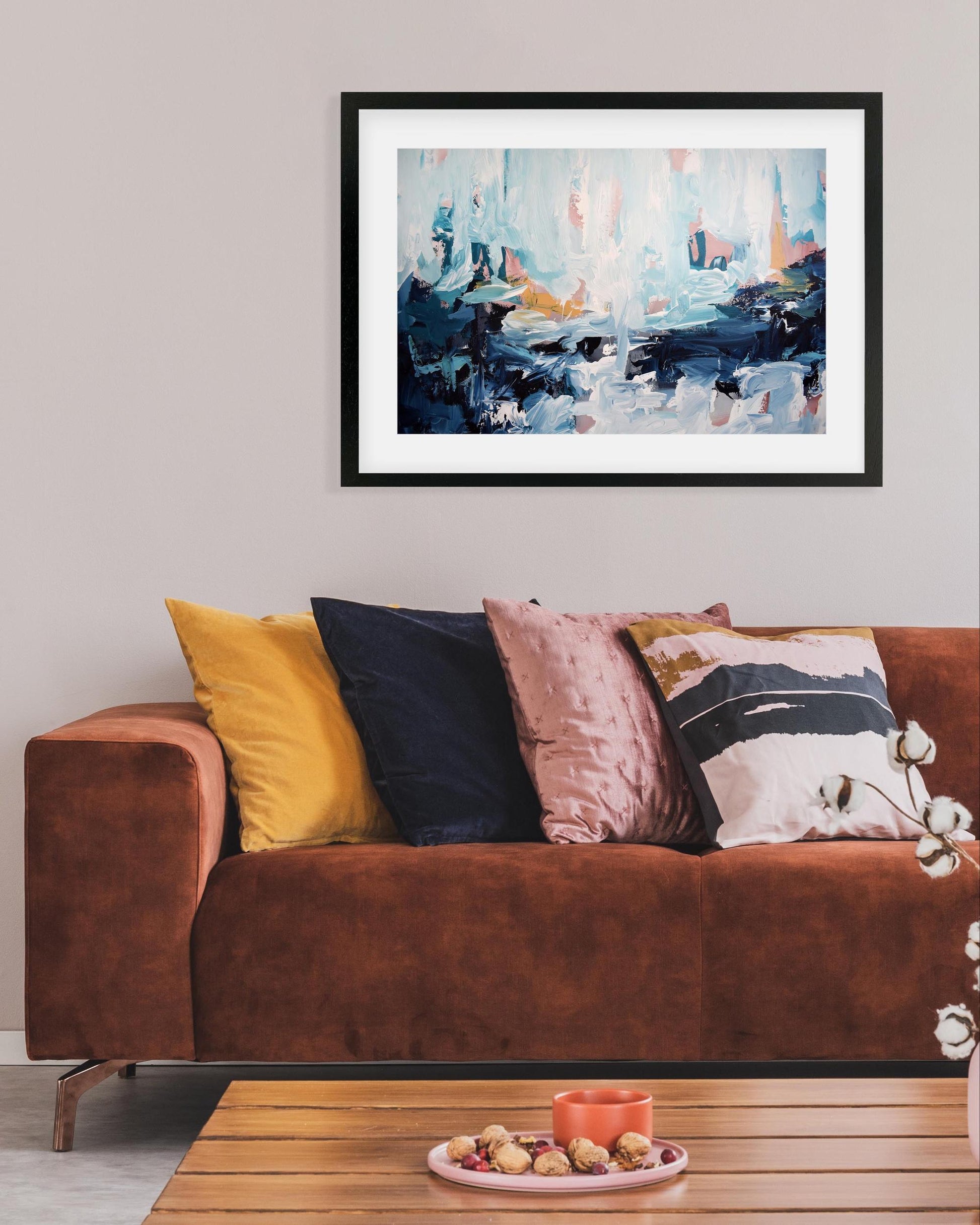 Living room with a brown sofa, colorful pillows, and a framed abstract painting on the wall.