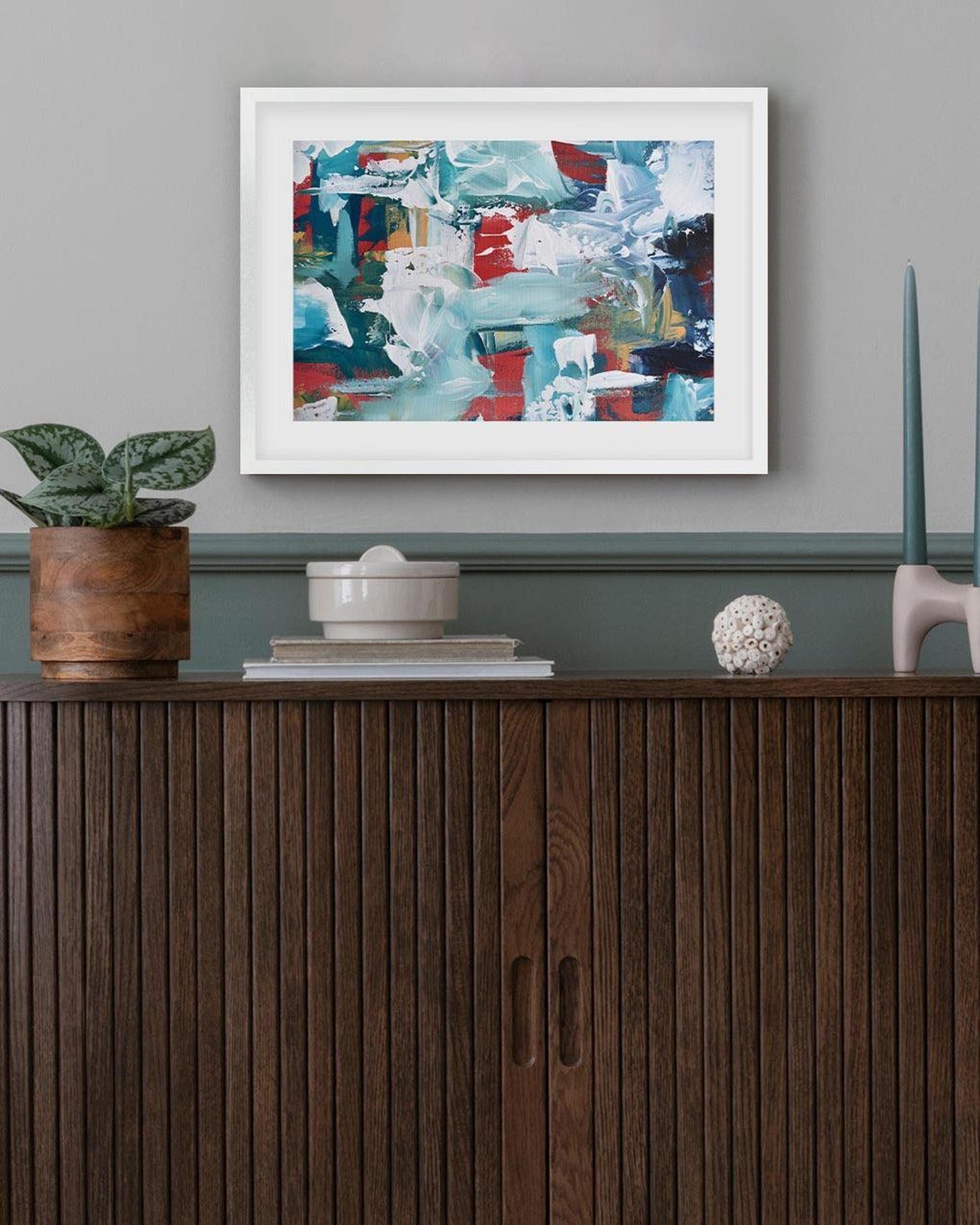 Abstract painting on a wall above a wooden cabinet with decorative items.