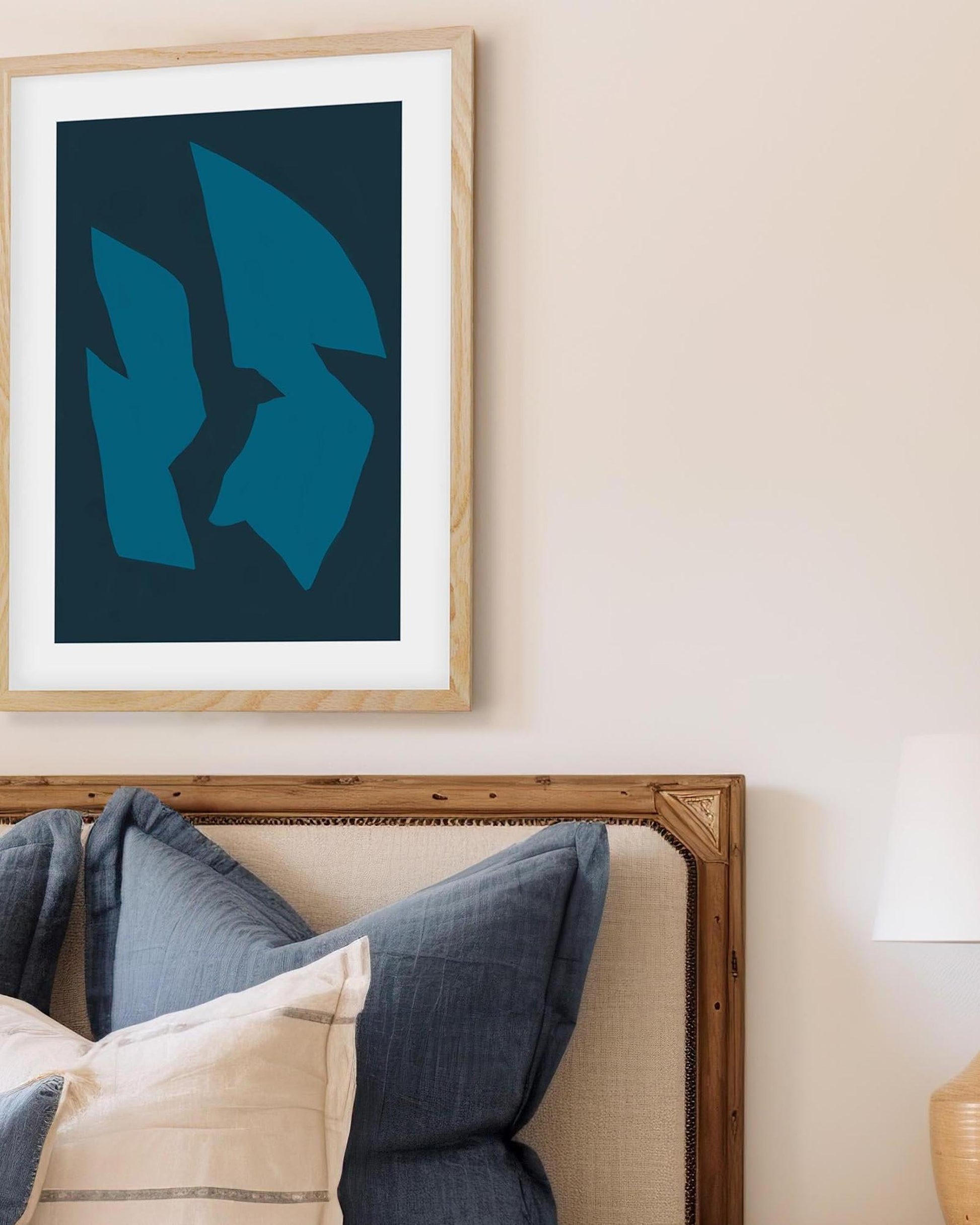 Framed abstract art piece on a wall above a bed with pillows.
