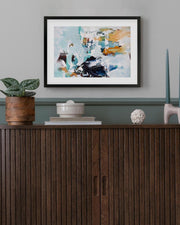 Framed abstract art on a wall above a wooden cabinet with decorative items.