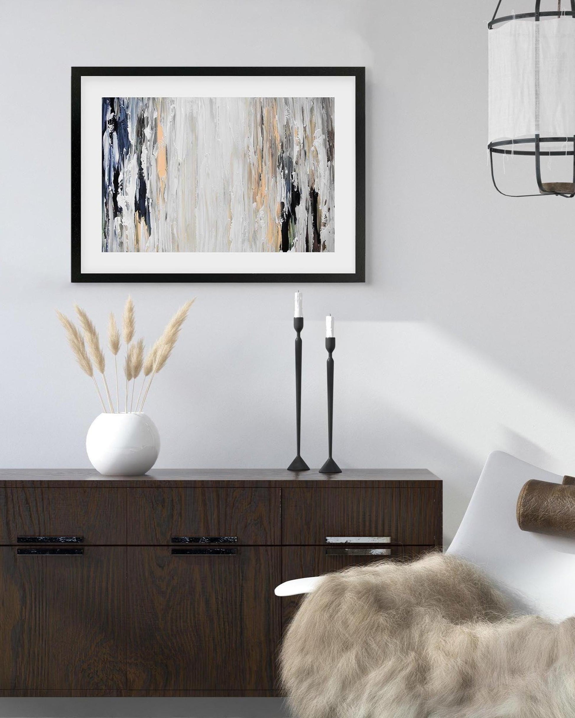Modern interior with abstract art, candles, and decorative items on a wooden cabinet.