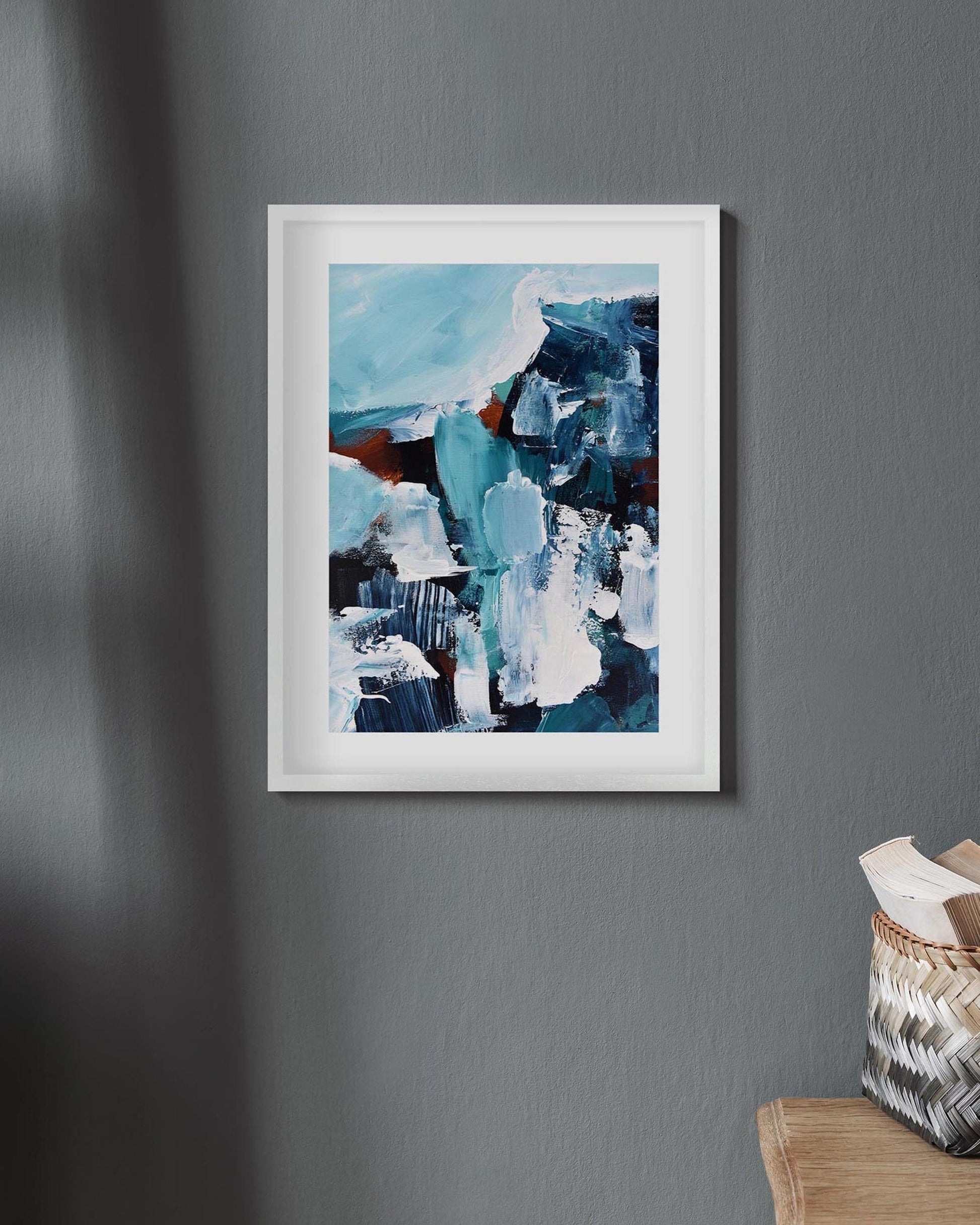 Abstract art print in a white frame on a gray wall with a wooden ladder and basket in the corner.