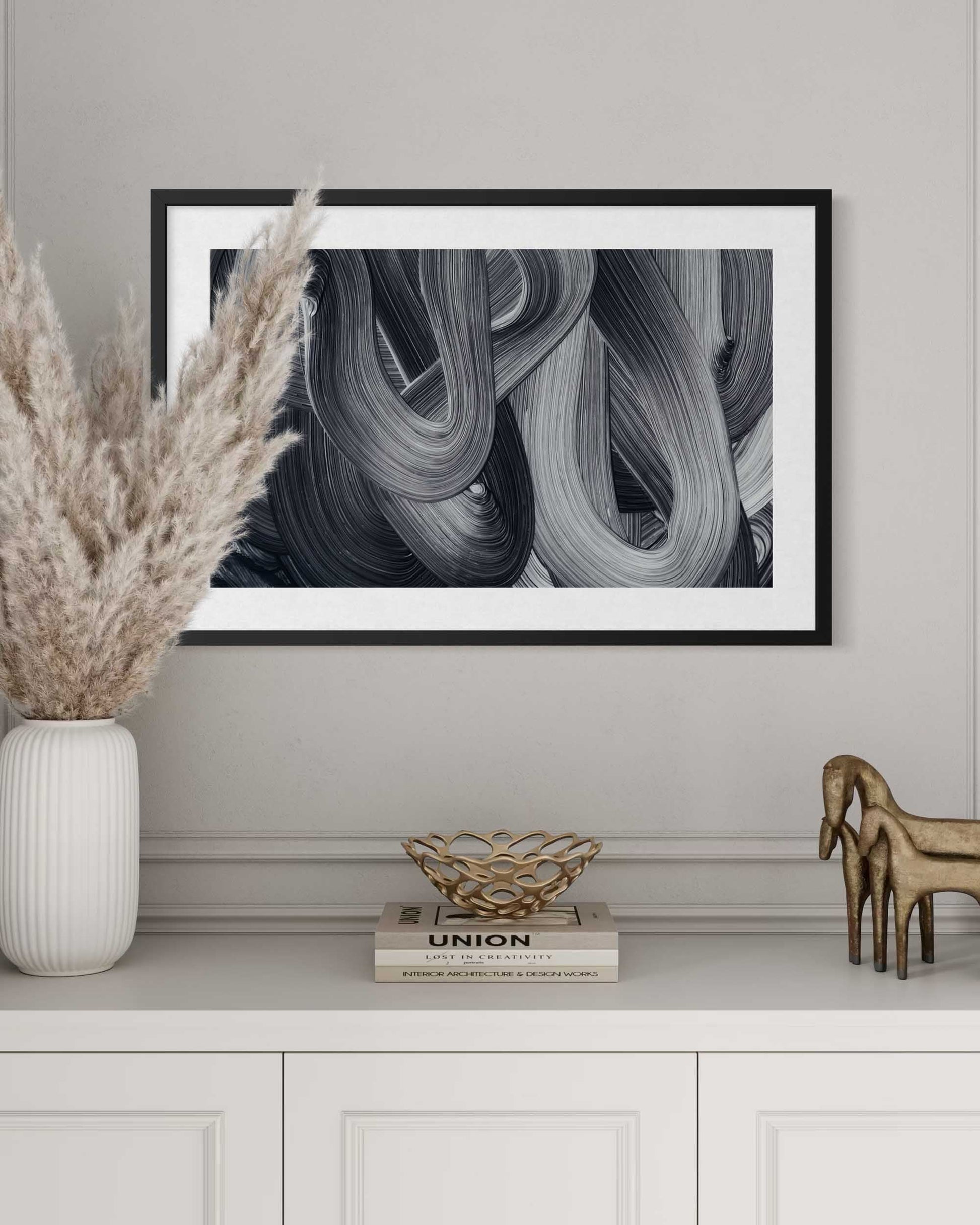 Framed abstract art piece on a wall above a white cabinet with decorative items.