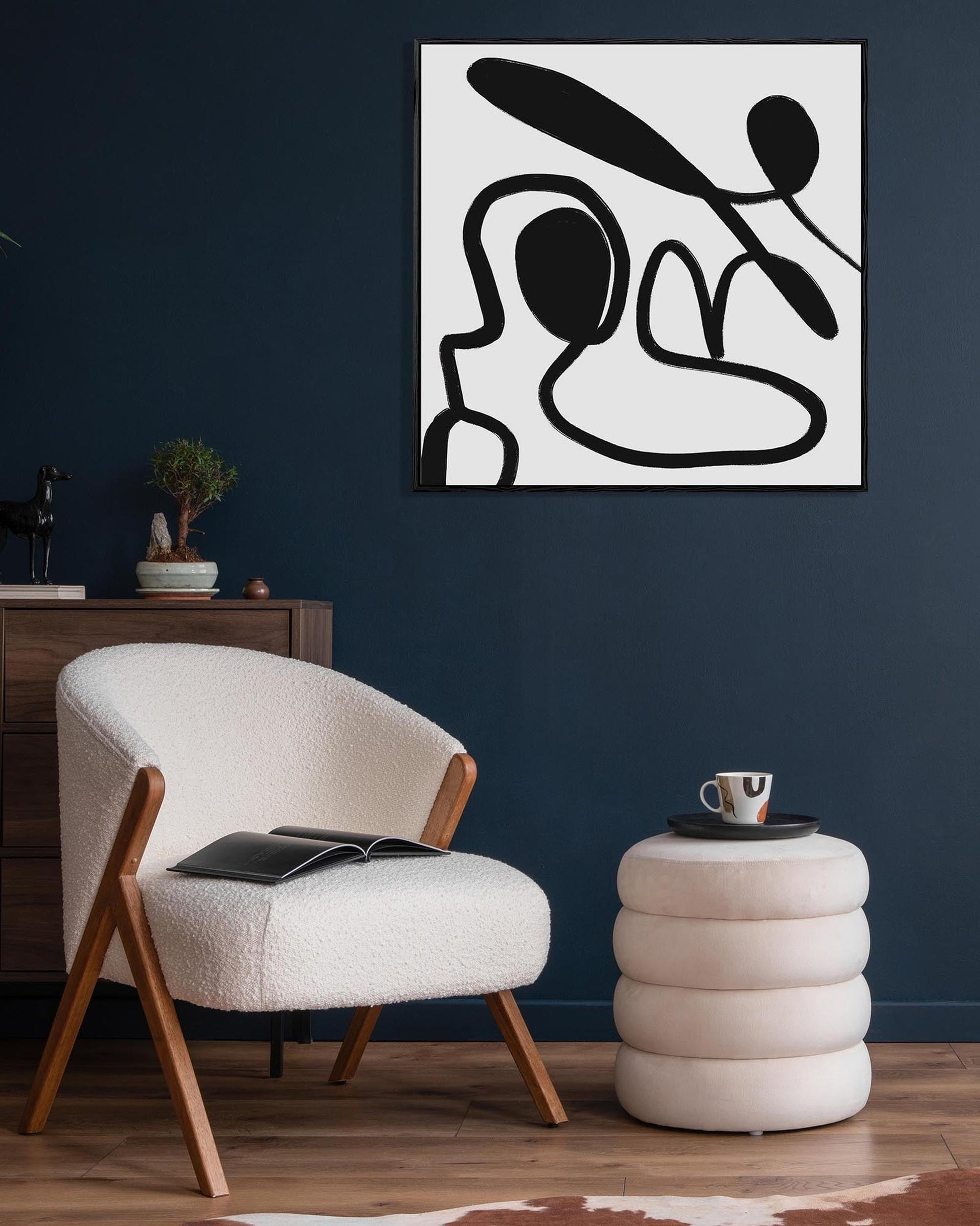 Modern living room with a white armchair, side table, and abstract artwork on a dark blue wall.